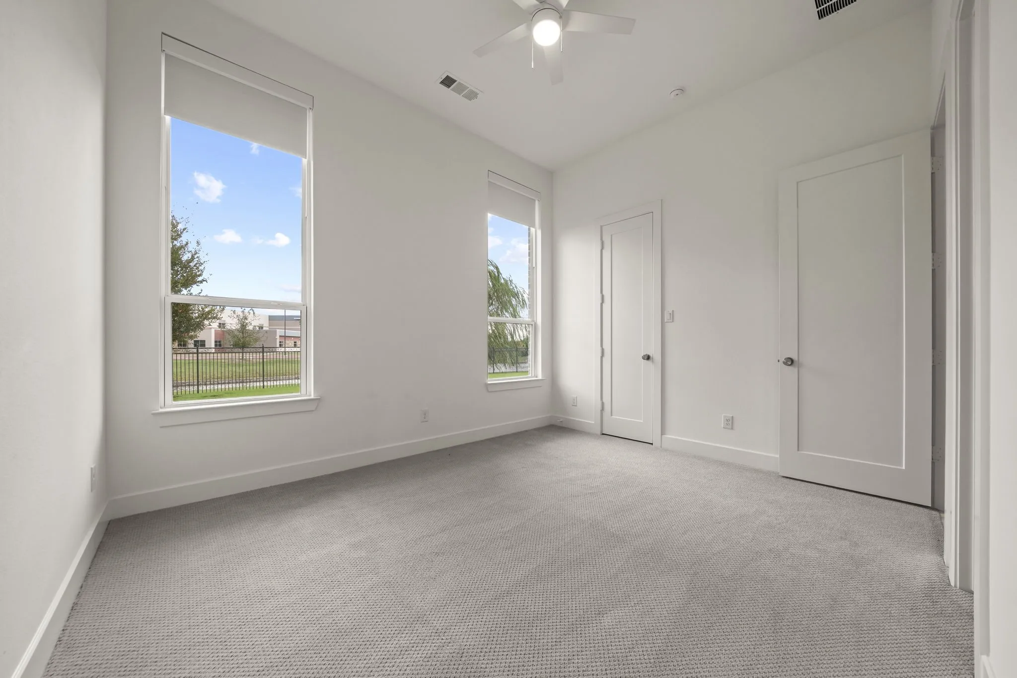 High ceilings, neutral carpeting, dual large windows, and a ceiling fan with integrated lighting