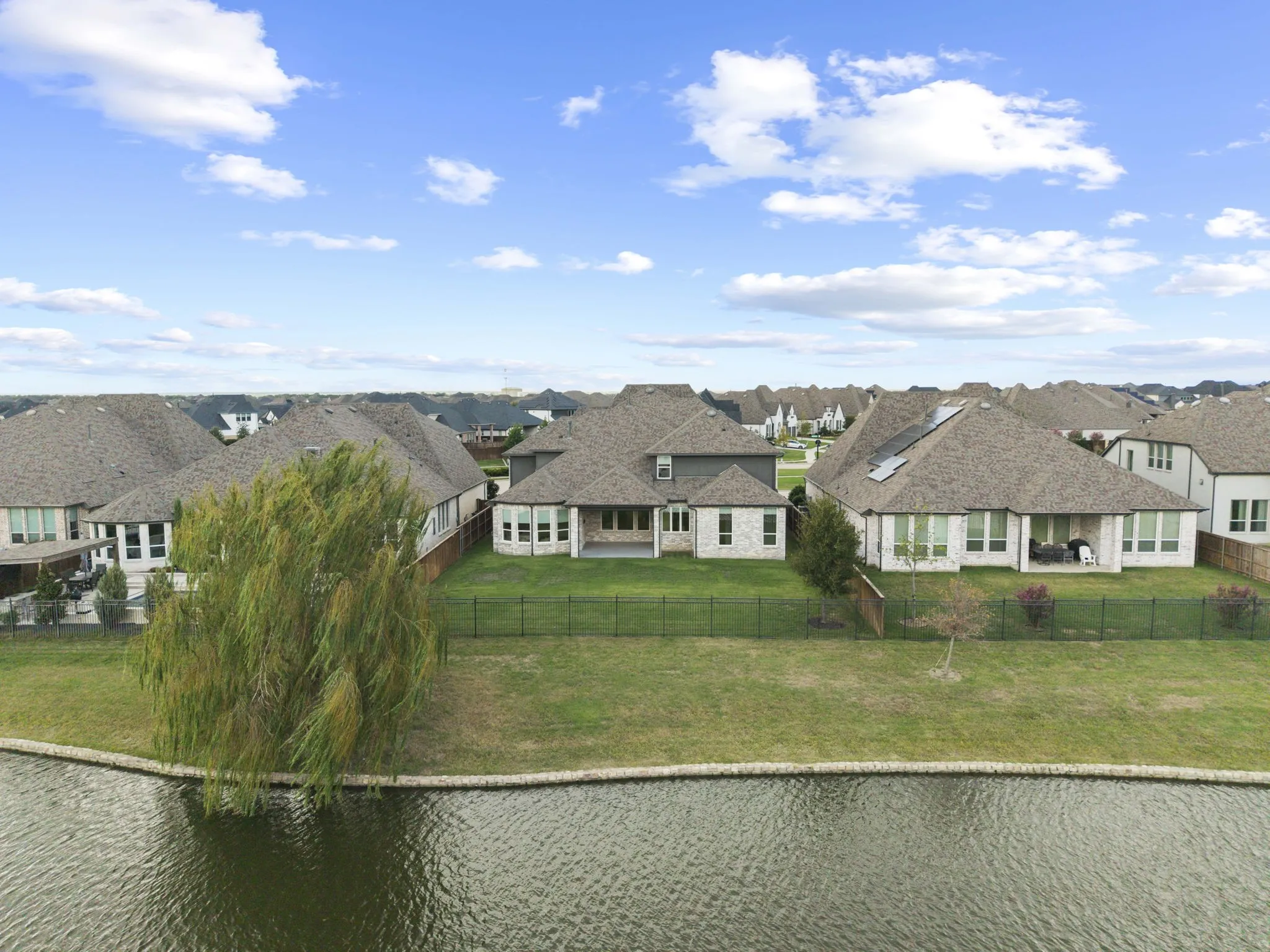 Multi-gabled masonry exterior with a covered rear patio, positioned on a waterfront lot featuring a fenced backyard and a mature weeping willow