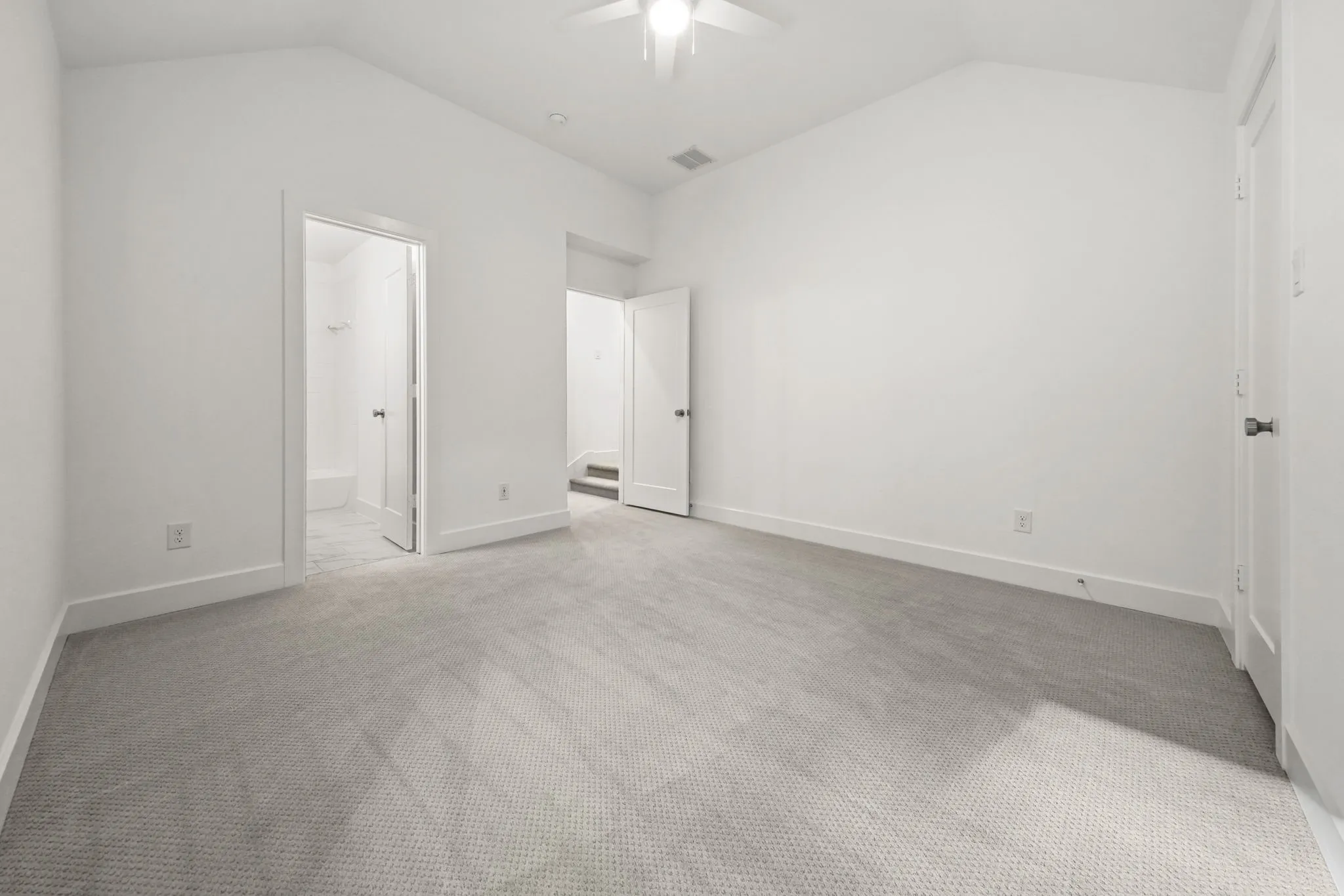 Vaulted ceiling featuring a central ceiling fan, neutral wall-to-wall carpeting, and solid-core interior doors