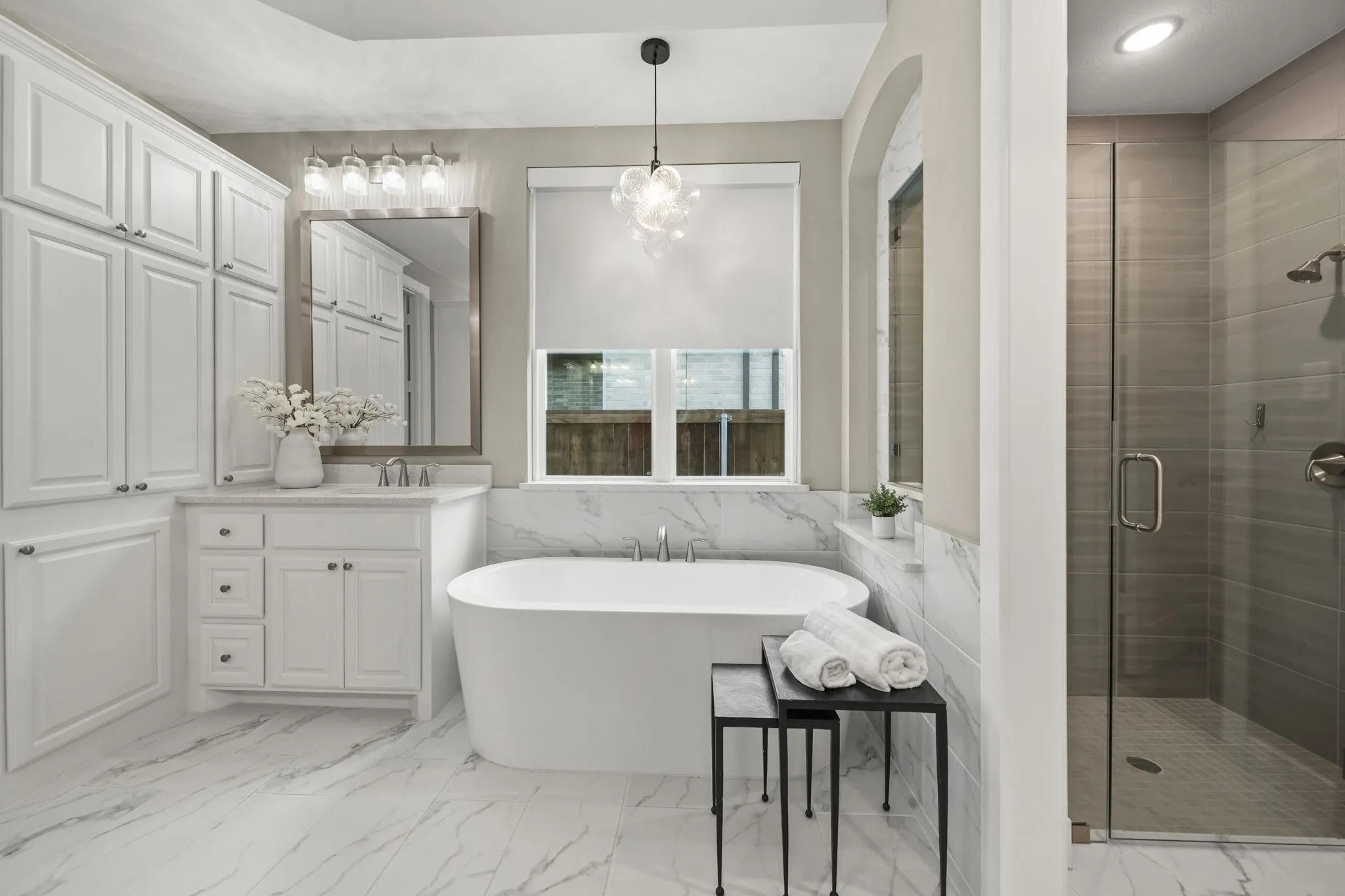 Freestanding soaking tub with stone-finish surround, white cabinetry, large-format tile flooring, and walk-in shower with glass enclosure