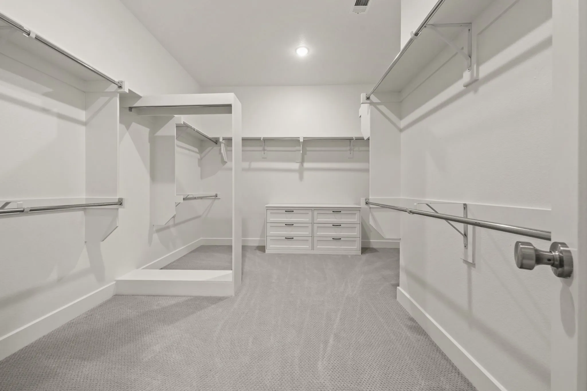 Walk-in closet featuring tiered shelving, built-in drawer cabinetry, integrated hanging rods, and wall-to-wall carpeting