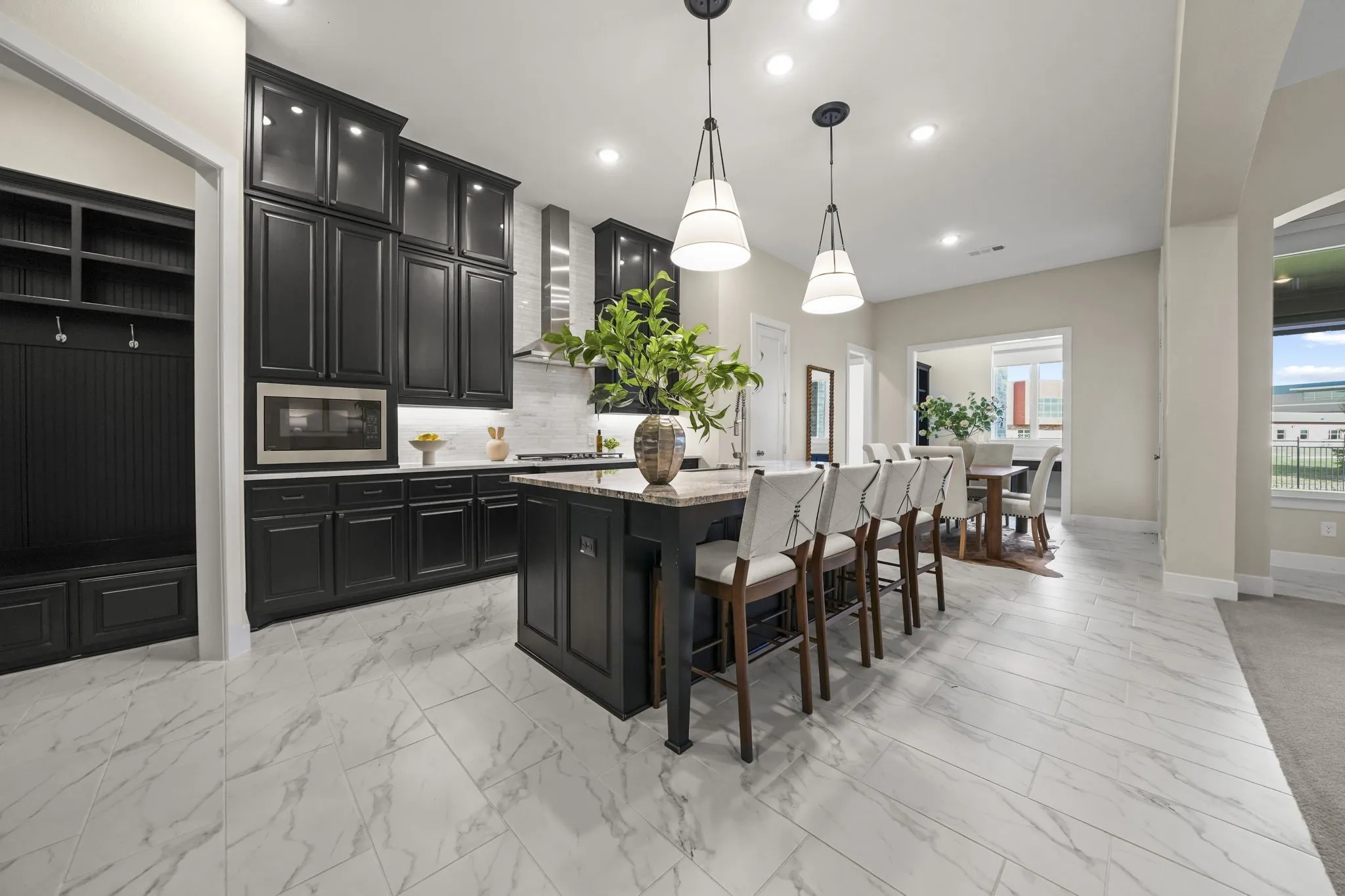 Kitchen featuring floor-to-ceiling dark cabinetry, stone-finish countertops, a central island, patterned tile flooring, and built-in mudroom storage