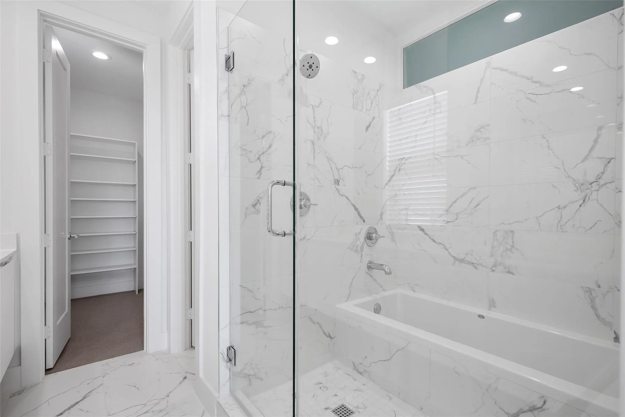 Bathroom featuring a walk-in shower with a frameless glass door, a deep soaking tub, and floor-to-ceiling stone-finish tile surround