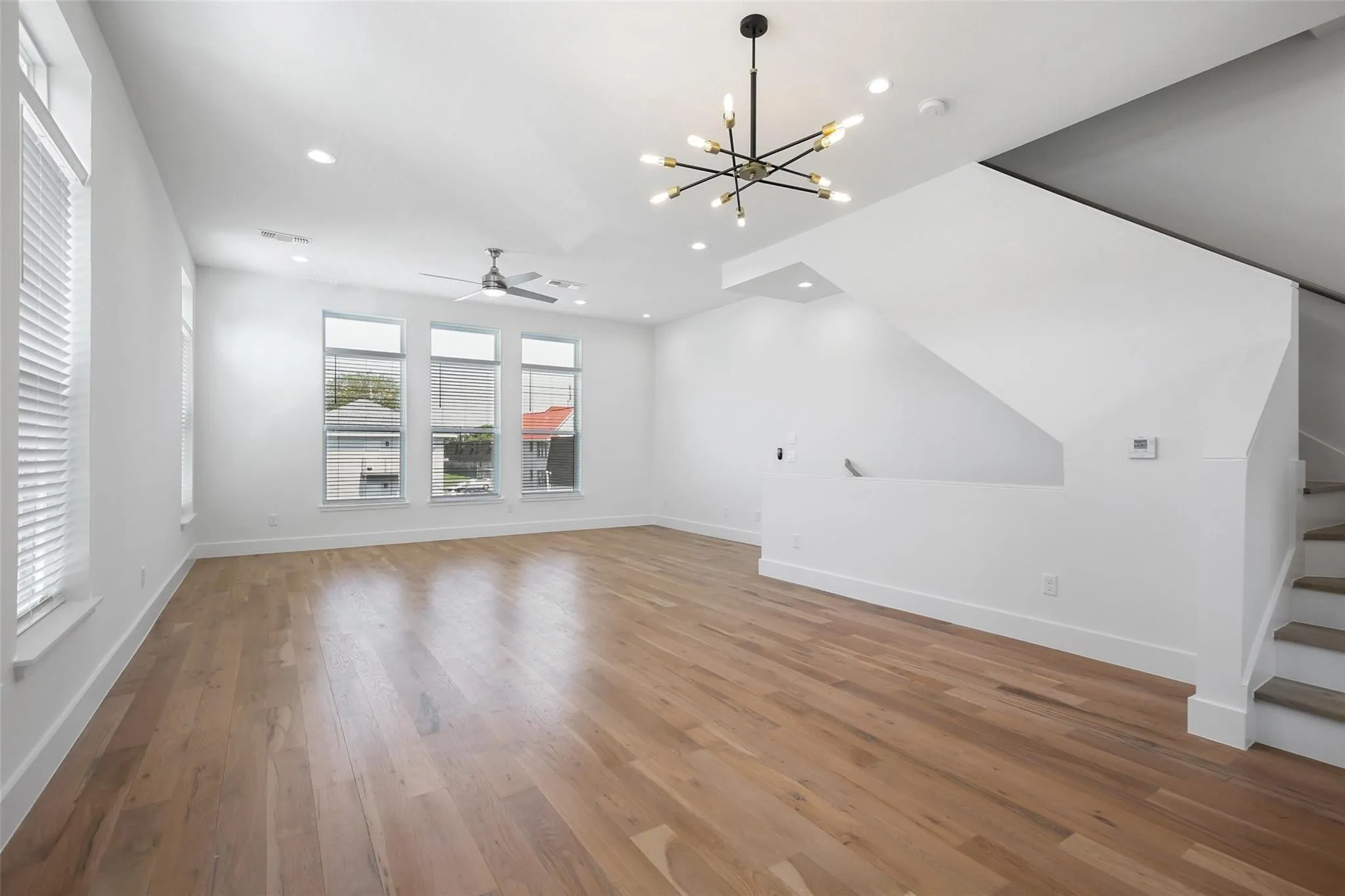 Open-concept interior featuring wood-finish flooring, multi-pane windows, a contemporary sputnik-style chandelier, a ceiling fan, and a staircase with wood-tread stairs