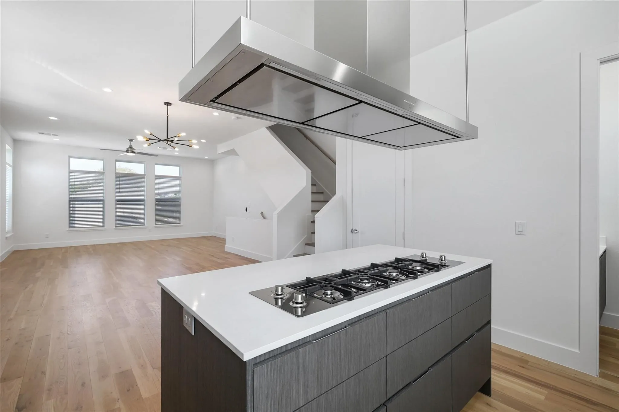 Kitchen island featuring quartz countertops, dark cabinetry, and an integrated gas cooktop, complemented by a stainless steel ceiling-mounted range hood, wood-finish flooring, and recessed lighting