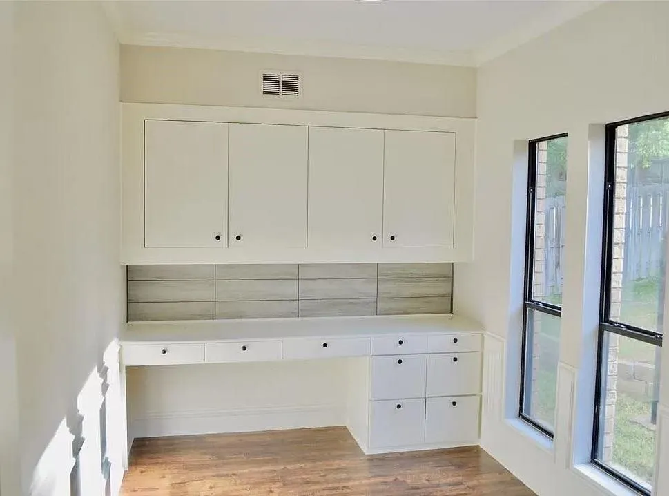 Built-in workstation featuring white cabinetry, soft-close hardware, a neutral horizontal tile backsplash, and wood-finish flooring with floor-to-ceiling windows
