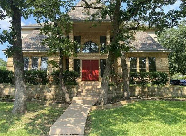 Brick exterior featuring a multi-gabled roofline, double-entry doors, arched transom window, and a stone retaining wall with a concrete walkway