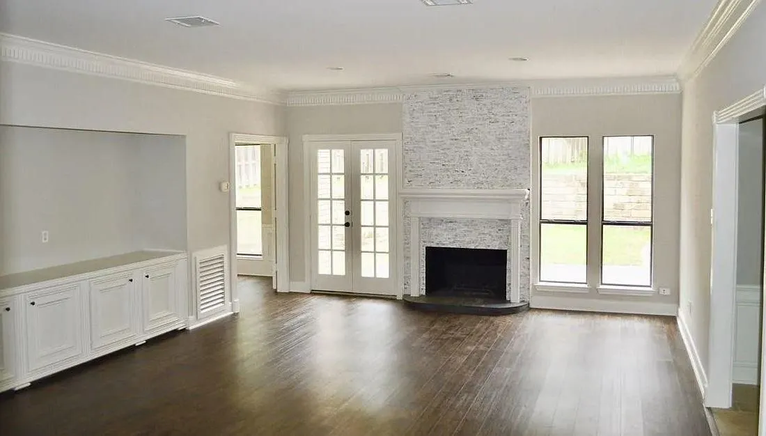 Living area featuring dark wood-finish flooring, built-in cabinetry, a floor-to-ceiling textured stone fireplace surround, crown molding, and glass-paneled double doors