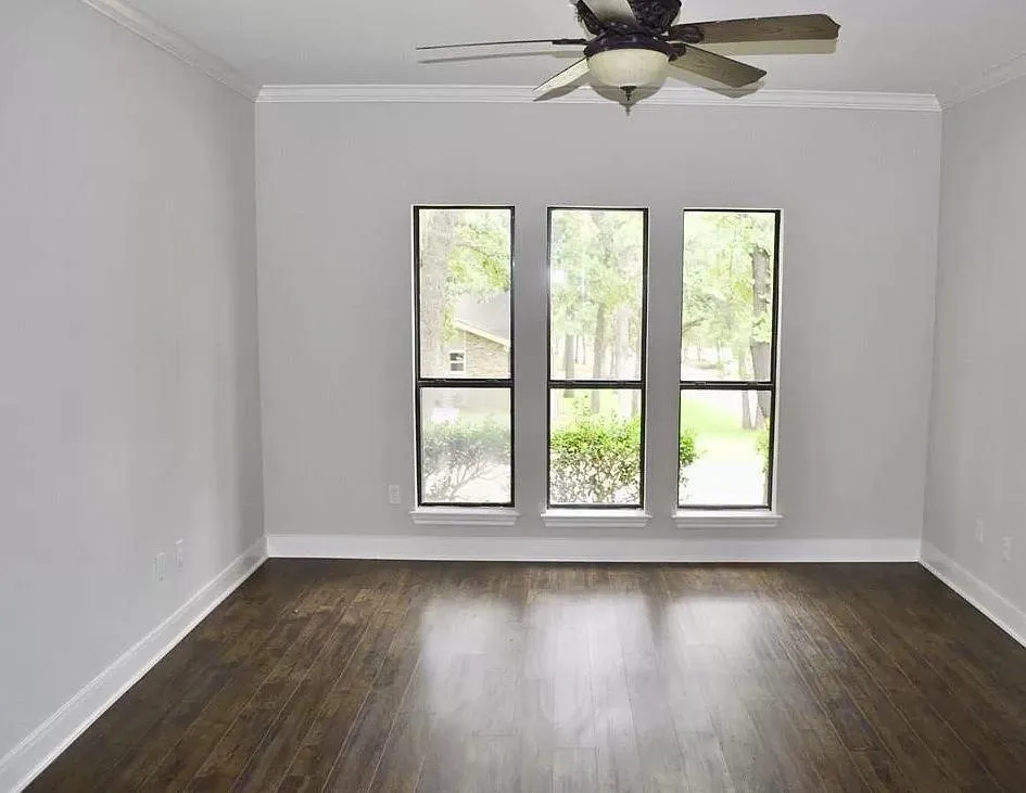 Room featuring wood-finish flooring, crown molding, three vertical windows, and a ceiling fan with integrated lighting