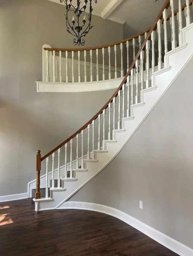 Curved staircase featuring white balusters, a natural wood-finish handrail, dark wood-finish flooring, and a decorative wrought iron chandelier
