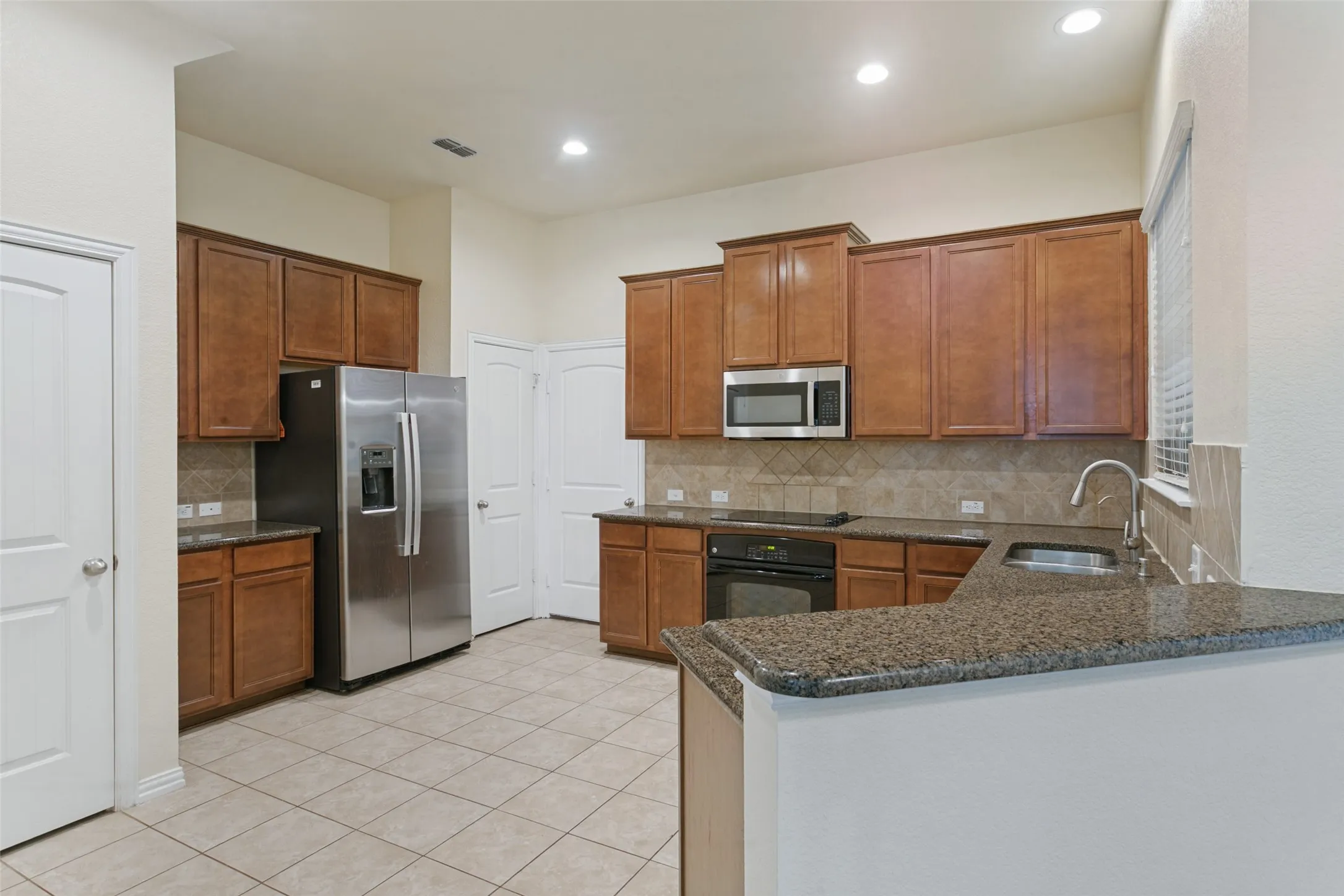 Kitchen featuring wood cabinetry, stone-surface countertops, tile backsplash, stainless steel refrigerator, and recessed lighting