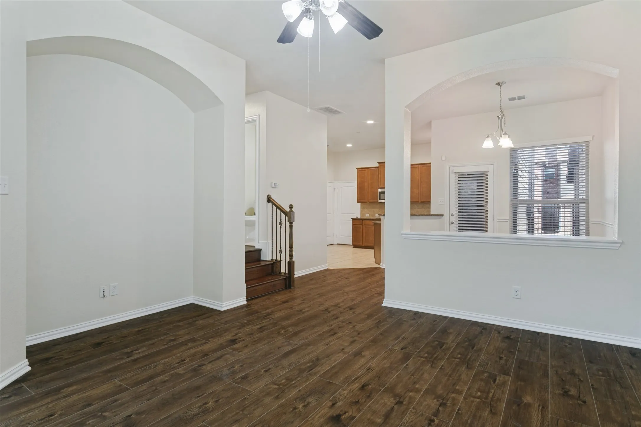 Interior space featuring wood-finish flooring, architectural arched openings, recessed lighting, a ceiling fan with integrated light fixture, and a staircase with a wooden handrail and metal balusters