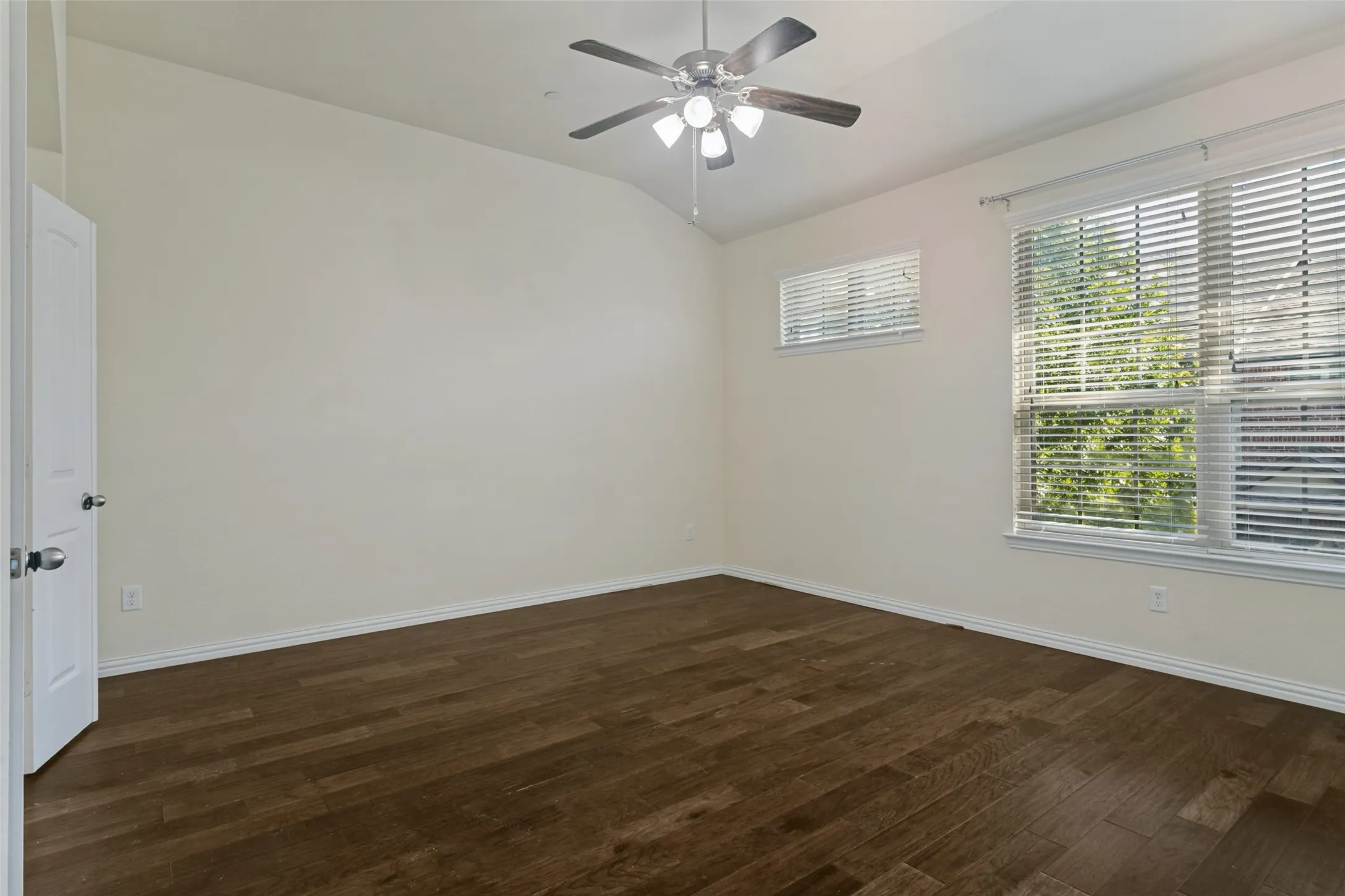 Vaulted ceiling with a central multi-light ceiling fan, wood-finish flooring, and multi-pane windows with horizontal blinds