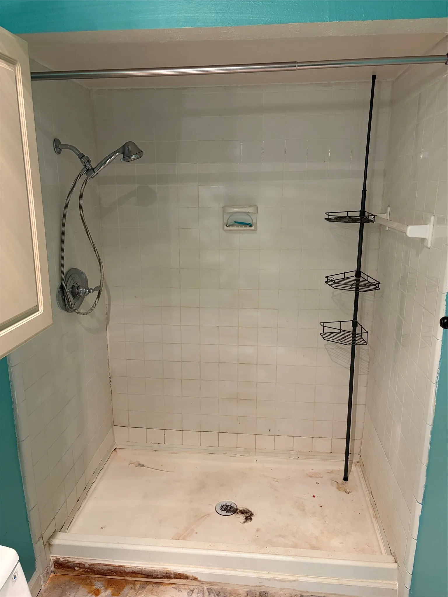 Shower stall featuring white wall tile, a metal shower head, an integrated soap dish, and a horizontal towel bar
