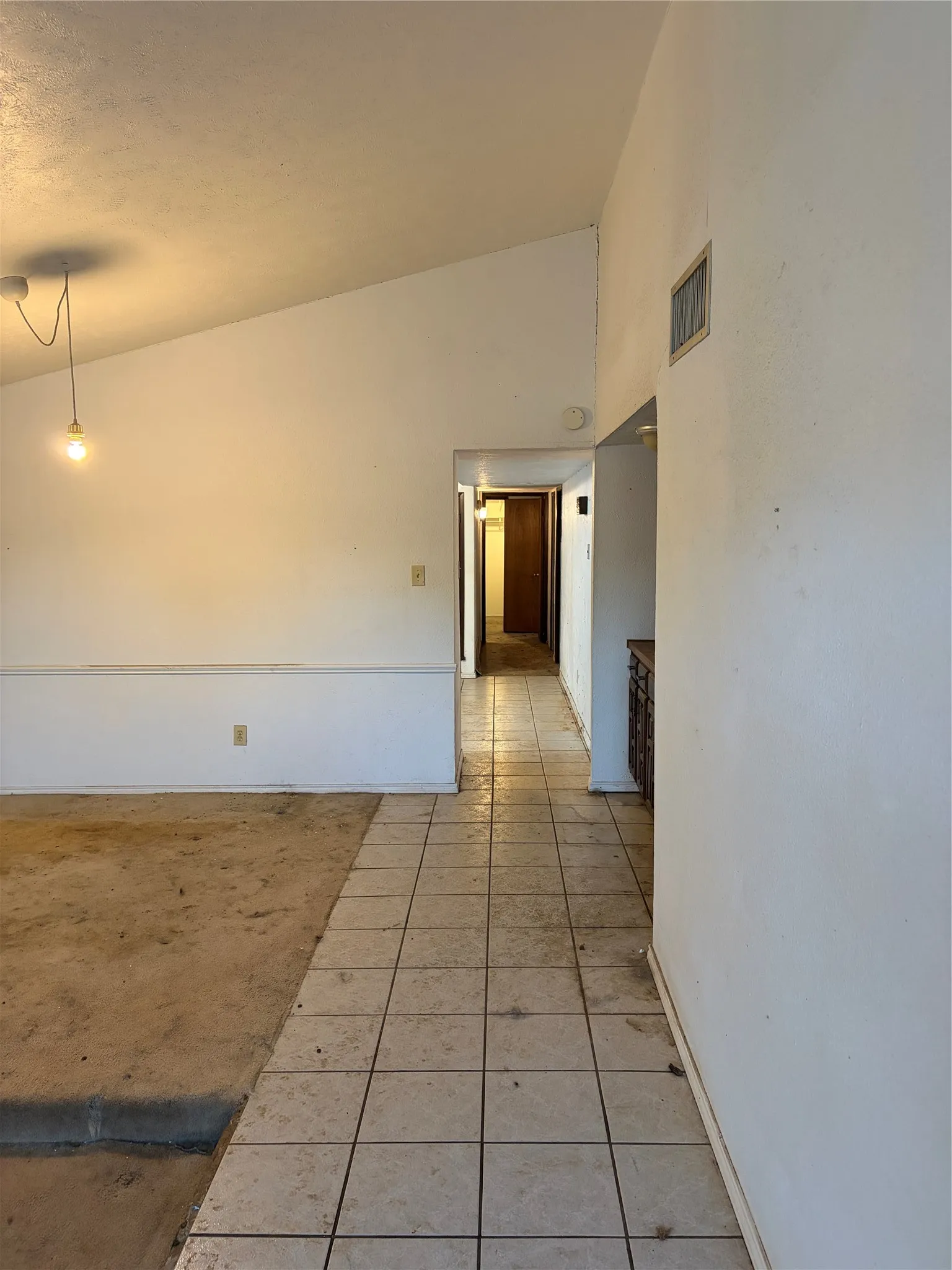 Vaulted ceilings featuring a pendant light fixture, ceramic tile flooring, and a chair rail