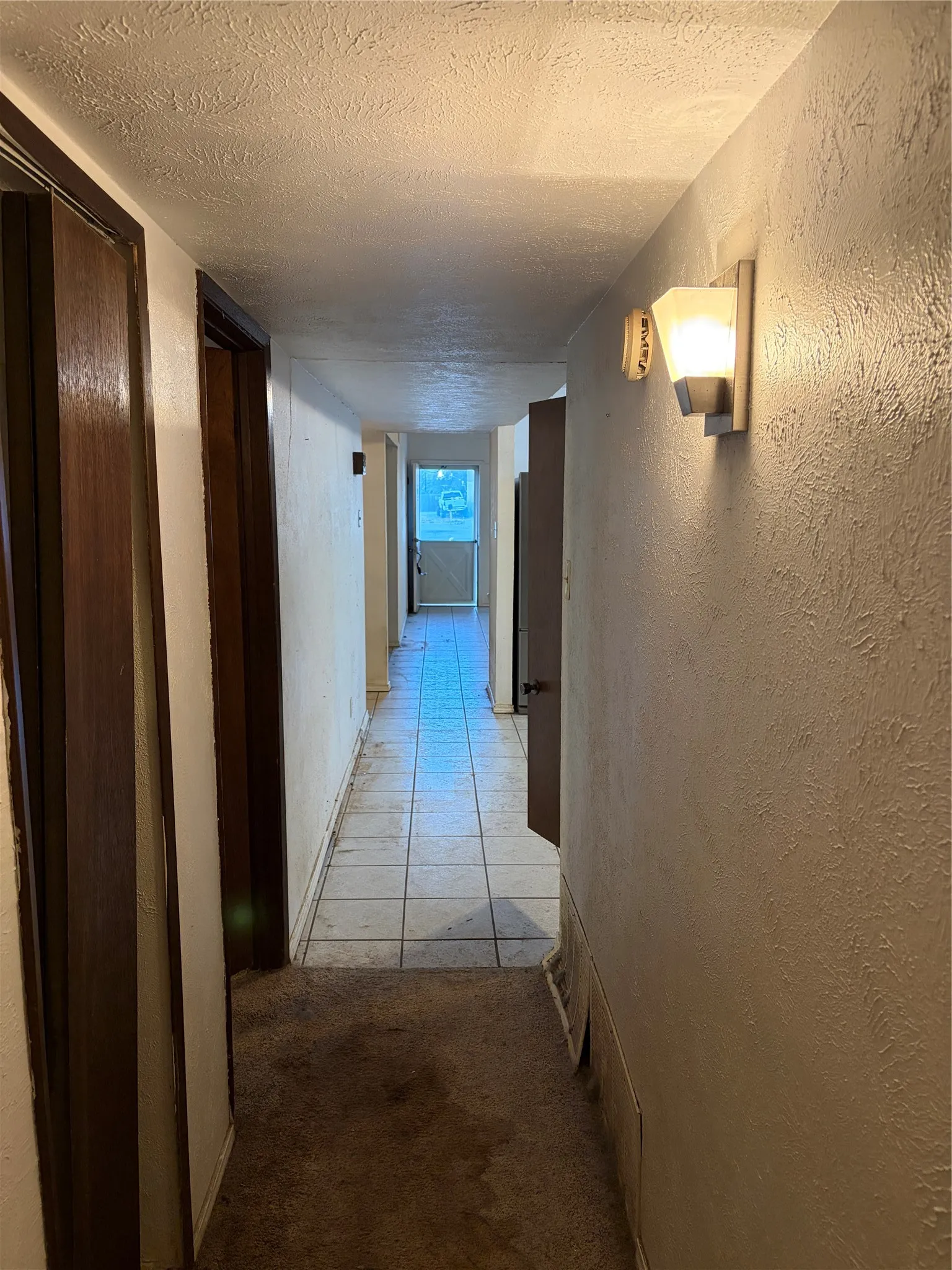 Hallway featuring textured wall finishes, tile flooring, and wall-mounted metal and frosted glass lighting fixtures