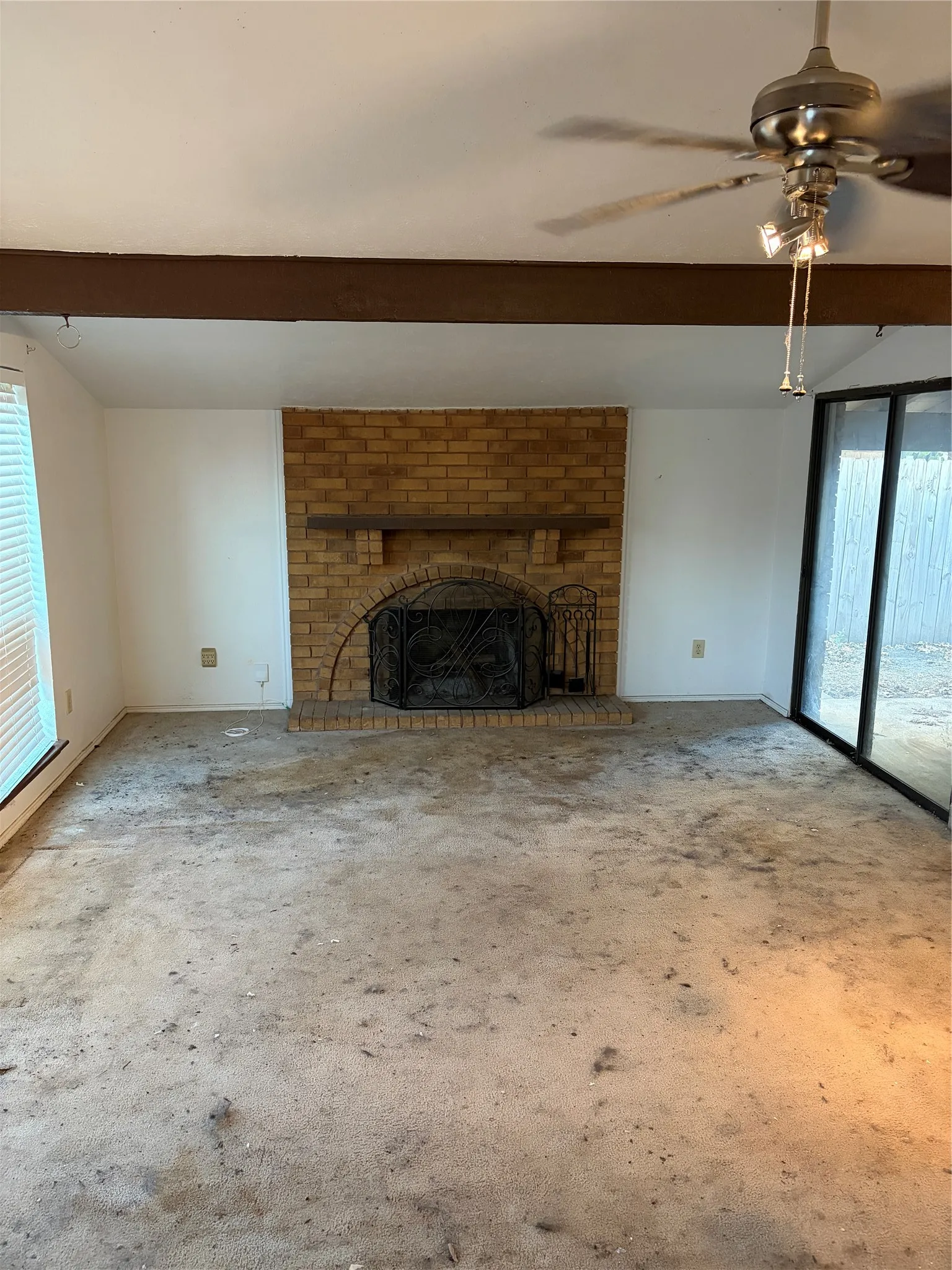 Interior featuring a brick fireplace with an arched hearth and mantle, exposed beam ceiling, sliding glass door, and a ceiling fan with integrated lighting