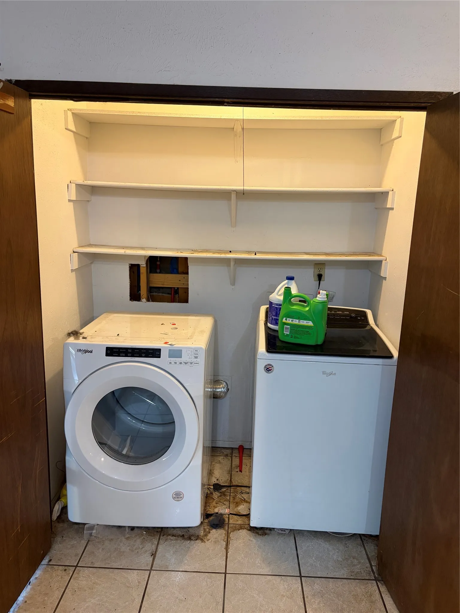 Laundry closet featuring three tiers of built-in white shelving and ceramic tile flooring