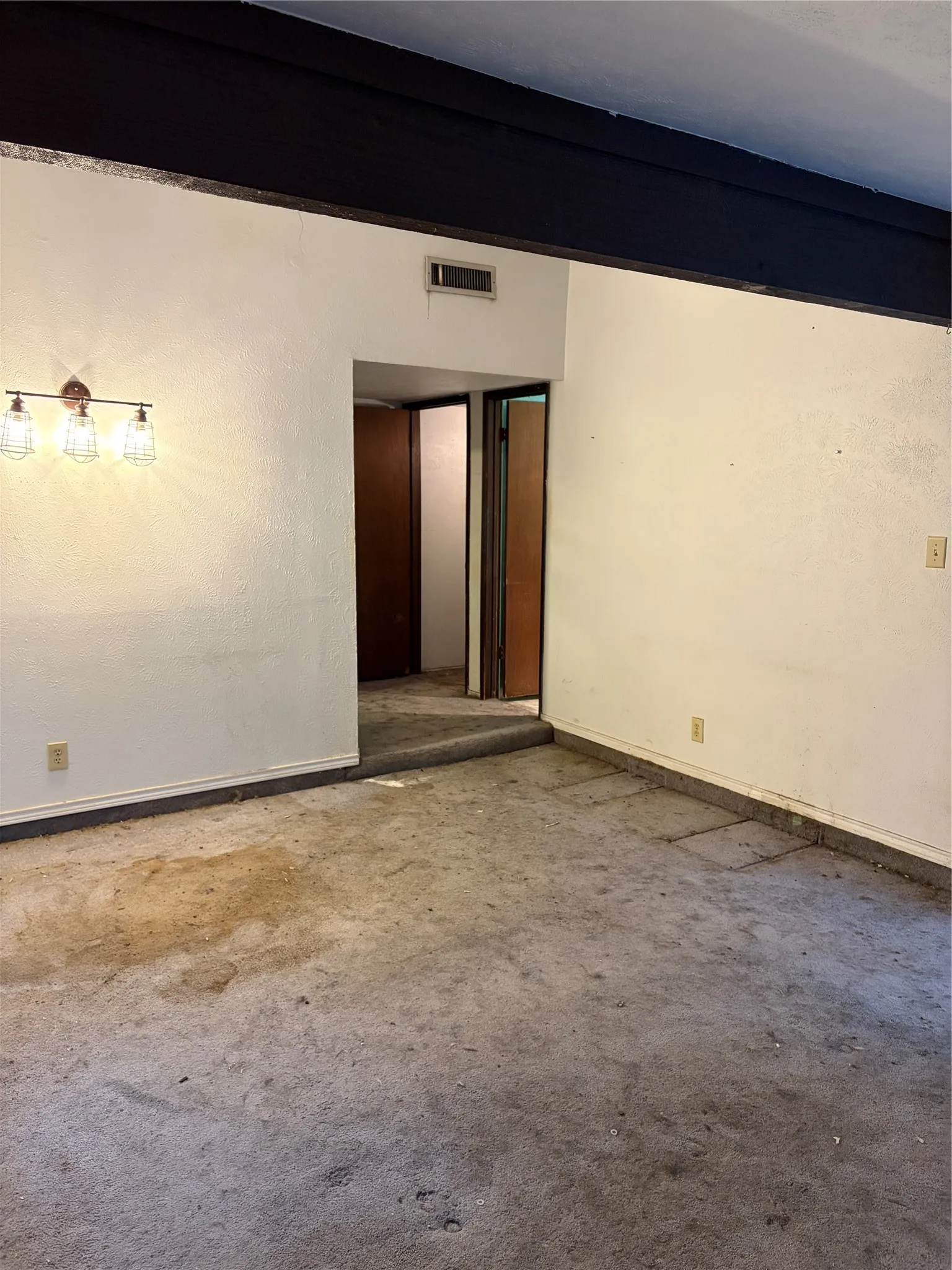 Exposed structural beam, wall-mounted three-light fixture with glass shades, and interior wood doors