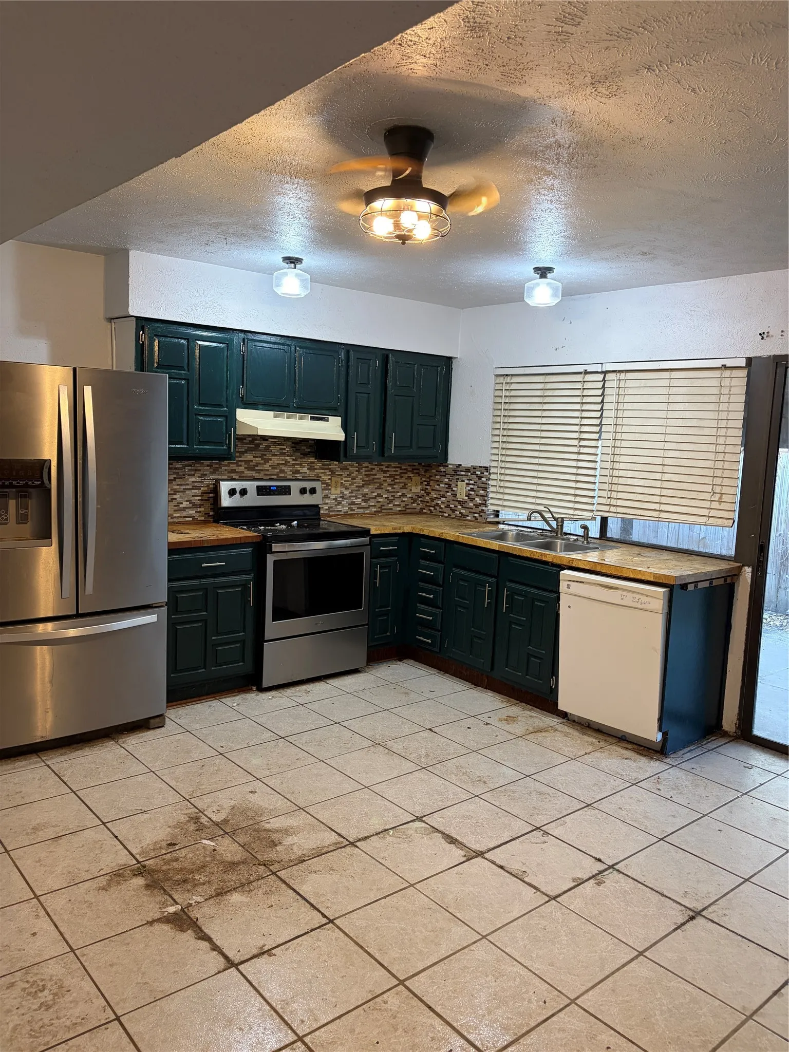 Kitchen featuring dark-finish cabinetry, stone-surface countertops, tile flooring, stainless steel appliances, and a ceiling fan with integrated lighting