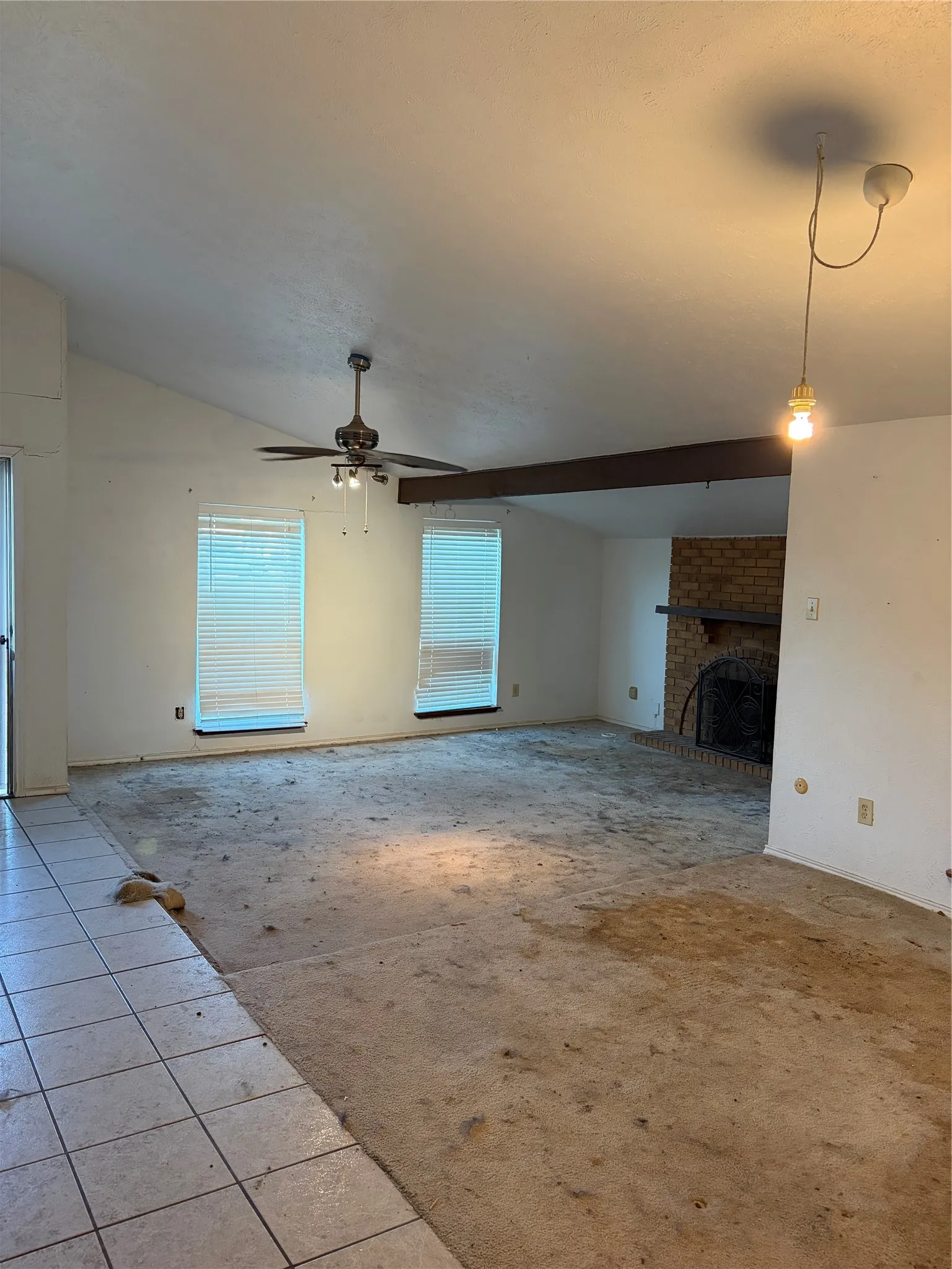 Vaulted ceilings with exposed structural beam, brick fireplace with mantel, ceiling fan, and ceramic tile flooring