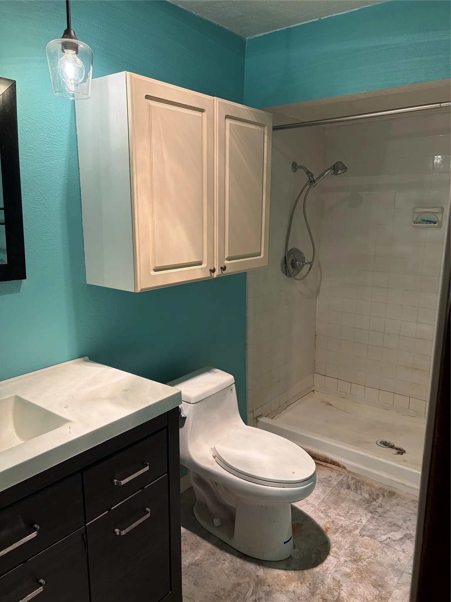 Dark wood-finish vanity with integrated sink, stone-surface countertop, white shaker-style wall cabinetry, single-piece toilet, and tile shower stall featuring a handheld fixture