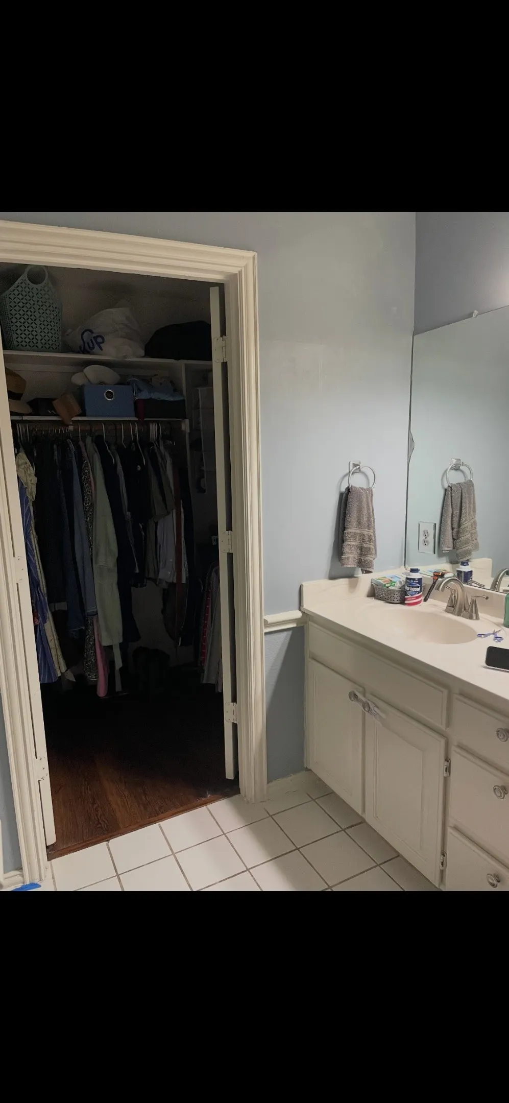 Bathroom featuring a vanity with integrated sink, expansive wall-mounted mirror, ceramic tile flooring, and a walk-in closet with built-in shelving