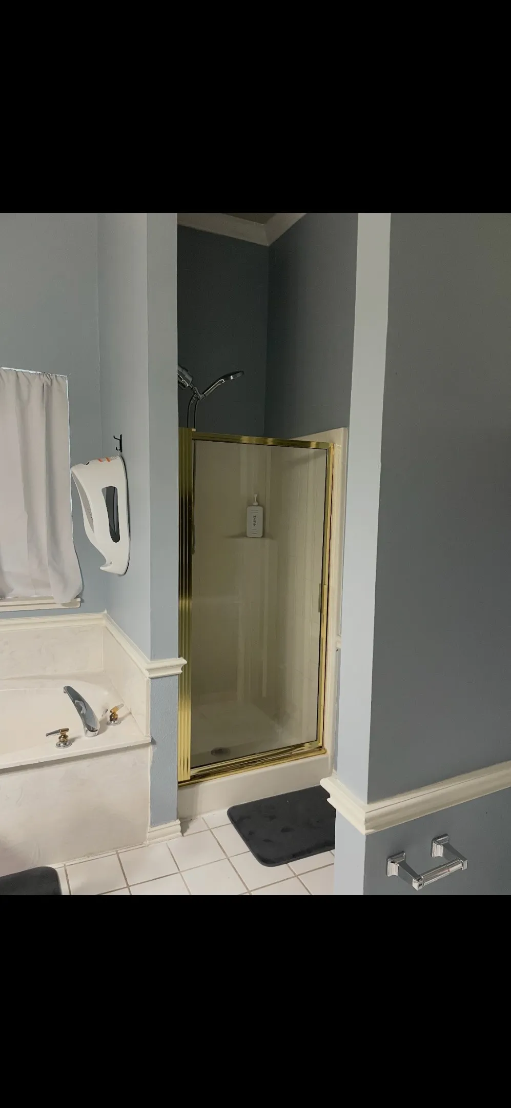 Bathroom featuring a jetted soaking tub with a tiled surround, a separate shower enclosure with a brass-finish frame, and tile flooring