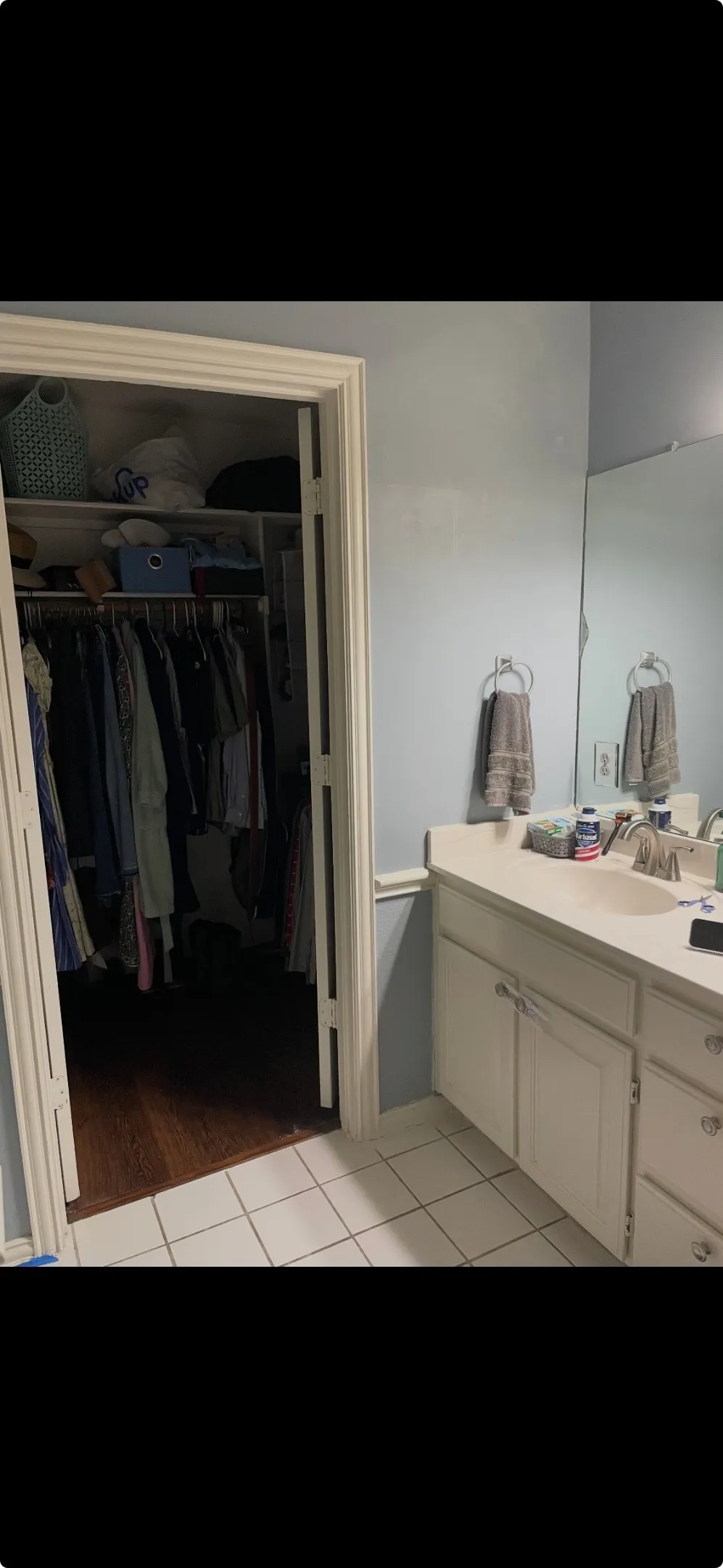 Vanity with integrated oval sink, solid-surface countertop, white cabinetry with hardware, large wall-mounted mirror, and tile flooring