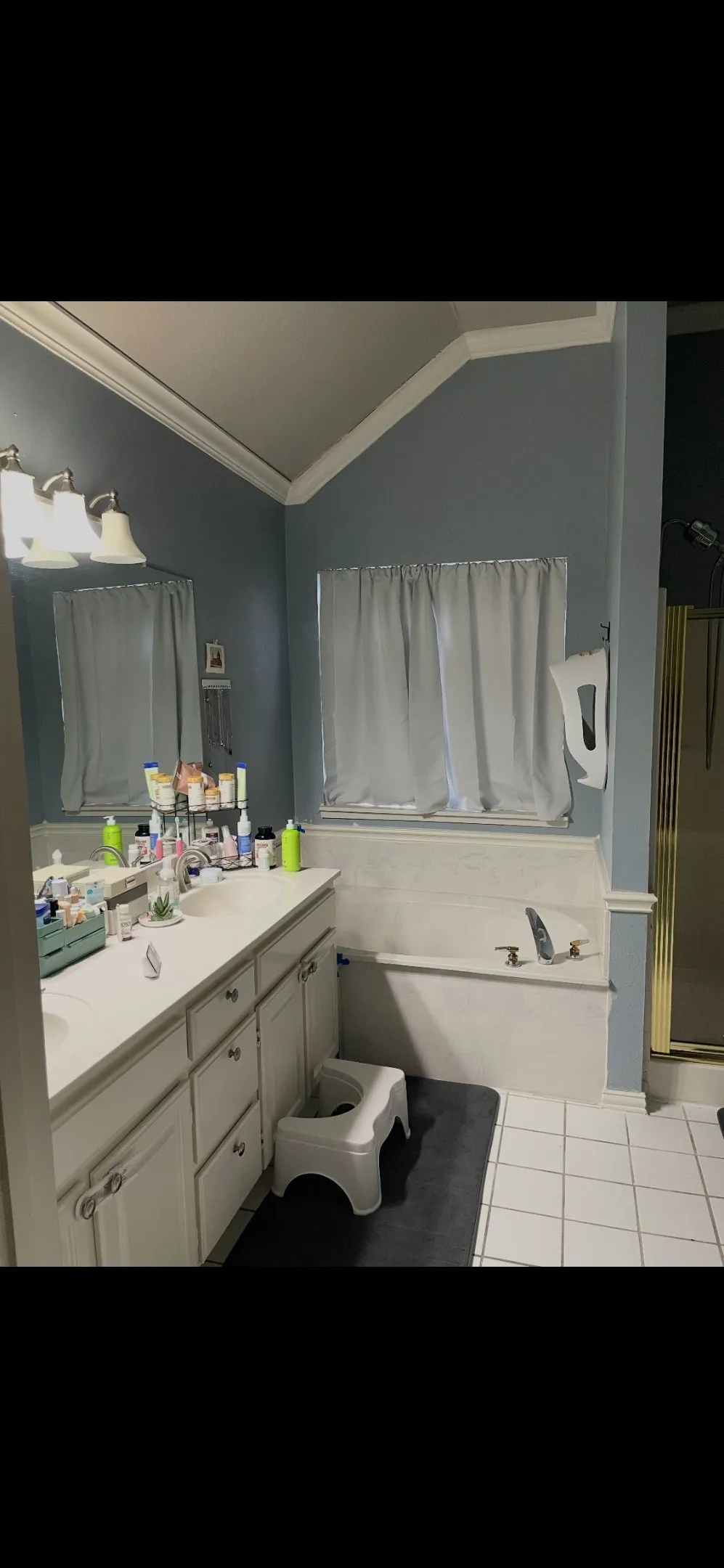 Bathroom featuring a dual-sink vanity with a solid-surface countertop, a built-in soaking tub, a vaulted ceiling, and ceramic tile flooring
