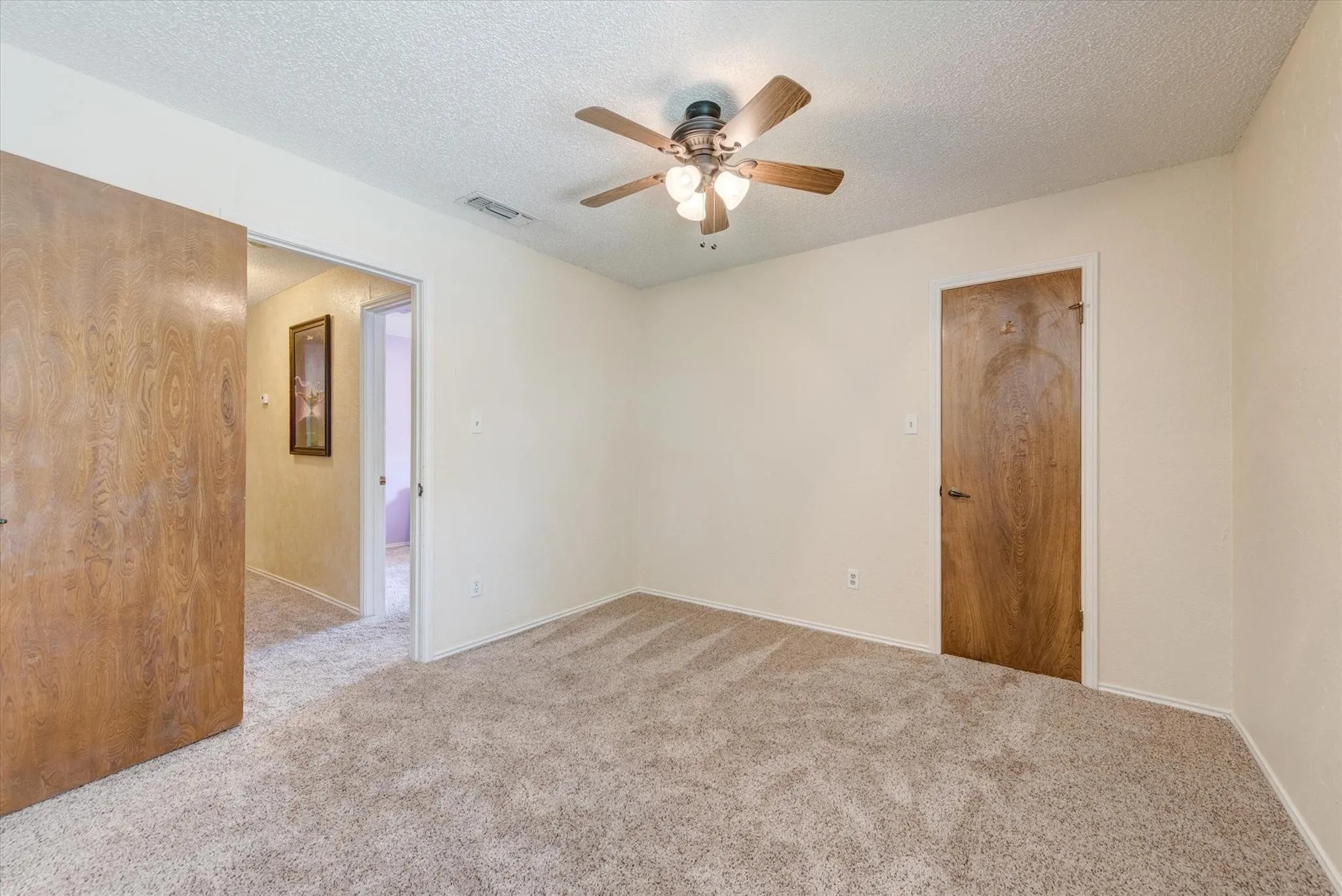 Room featuring neutral-toned carpeting, five-blade ceiling fan with integrated lighting, and wooden slab-style doors