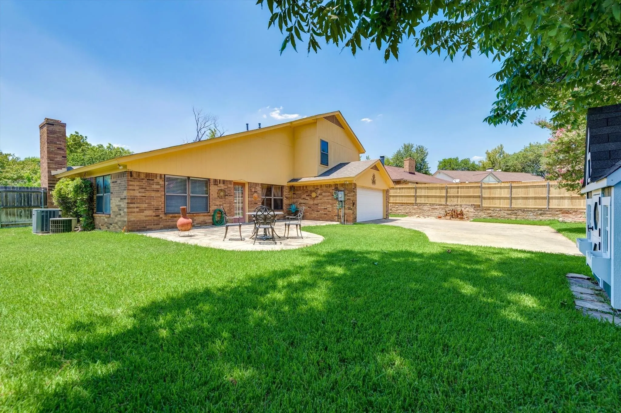 Exterior rear elevation featuring brick and stucco siding, a masonry chimney, a concrete patio, and a wood privacy fence