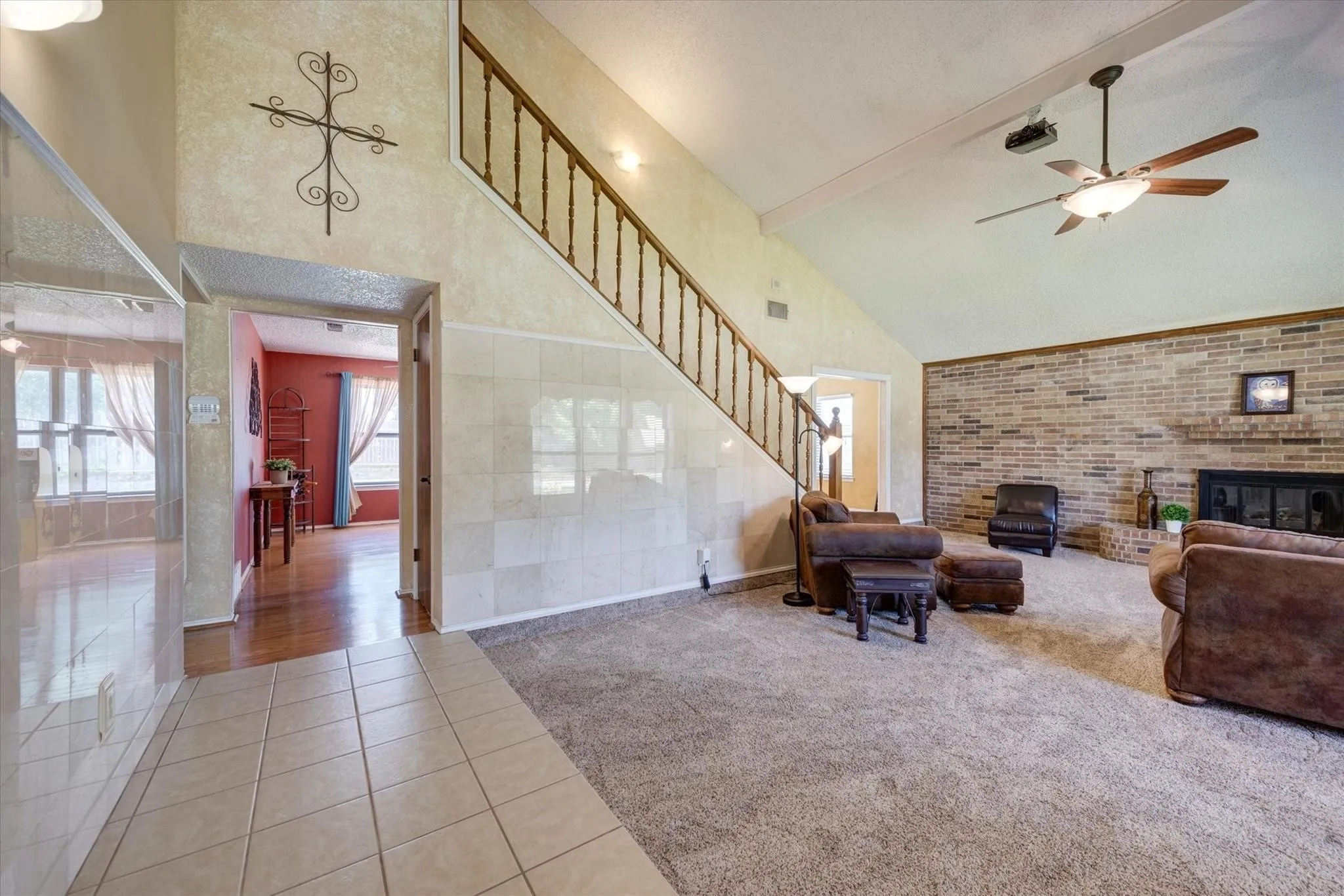 Vaulted ceiling featuring a central ceiling fan, floor-to-ceiling brick fireplace, and staircase with wooden balusters