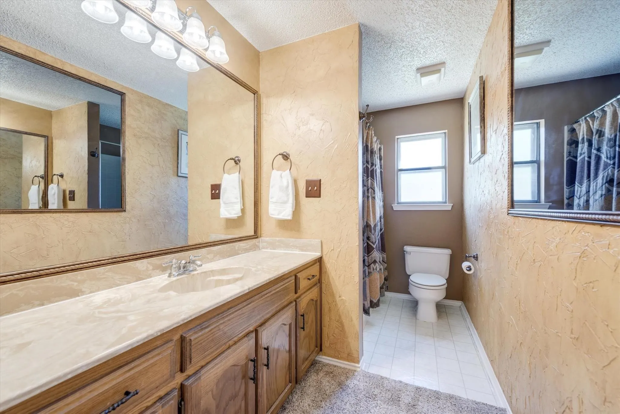 Bathroom featuring a vanity with wood cabinetry, a molded countertop with an integrated sink, a full-width wall mirror, and overhead light fixtures