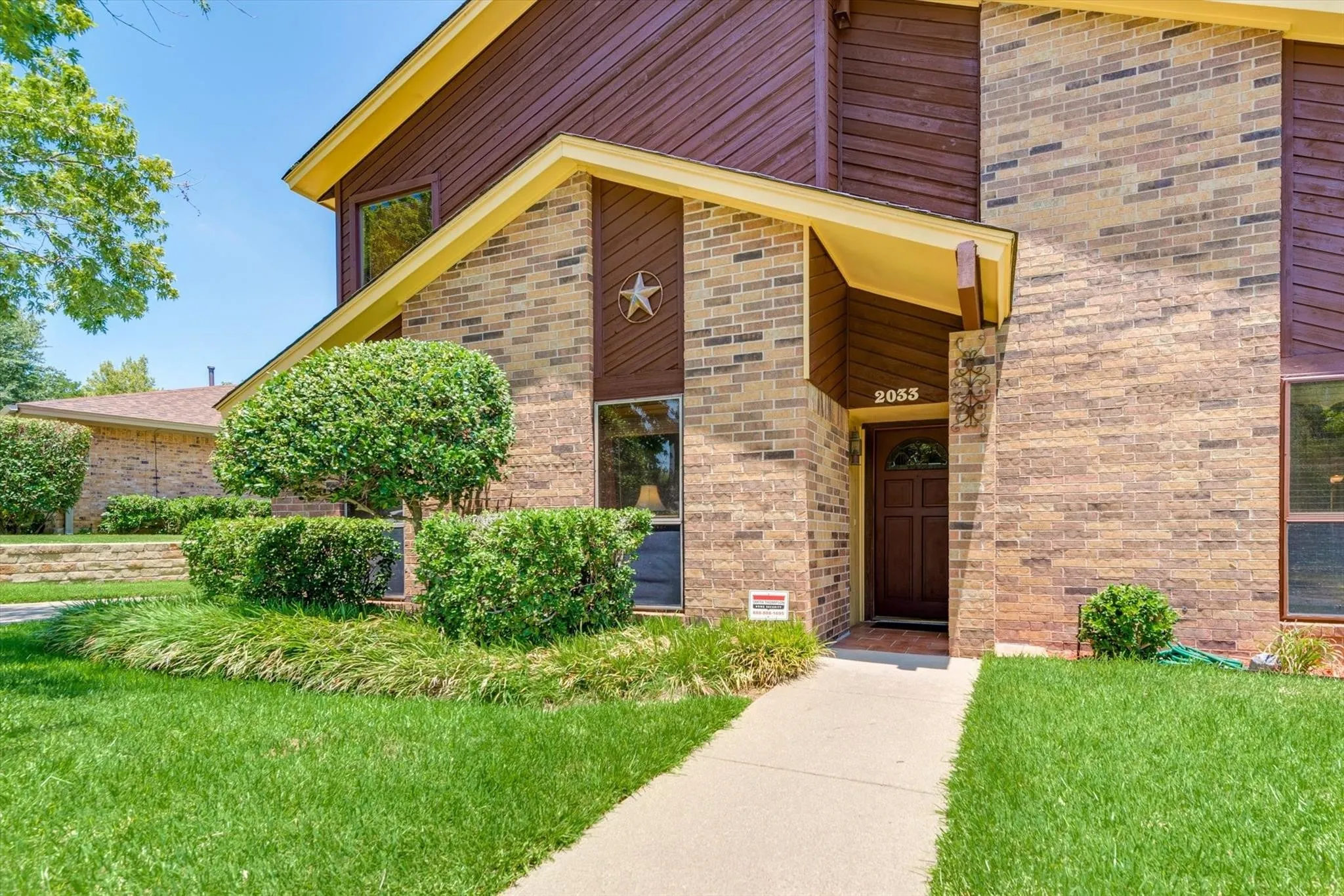 Multi-level exterior featuring light brick facade, dark wood-tone siding, decorative metal star accent, and a solid wood front door with a glass inlay
