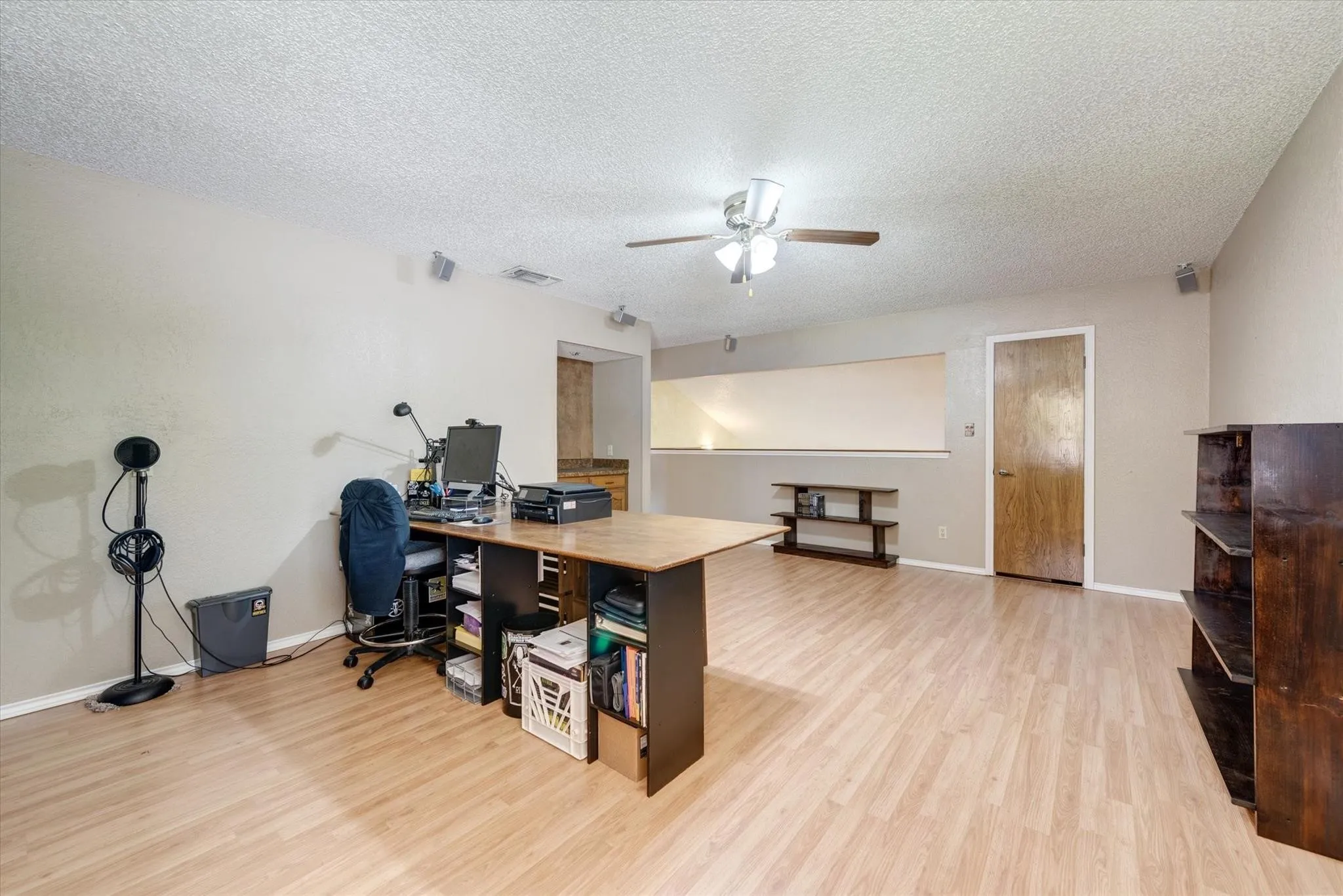 Open-concept room featuring light wood-finish flooring, a neutral color palette, a ceiling fan with integrated lighting, and a solid-core interior door