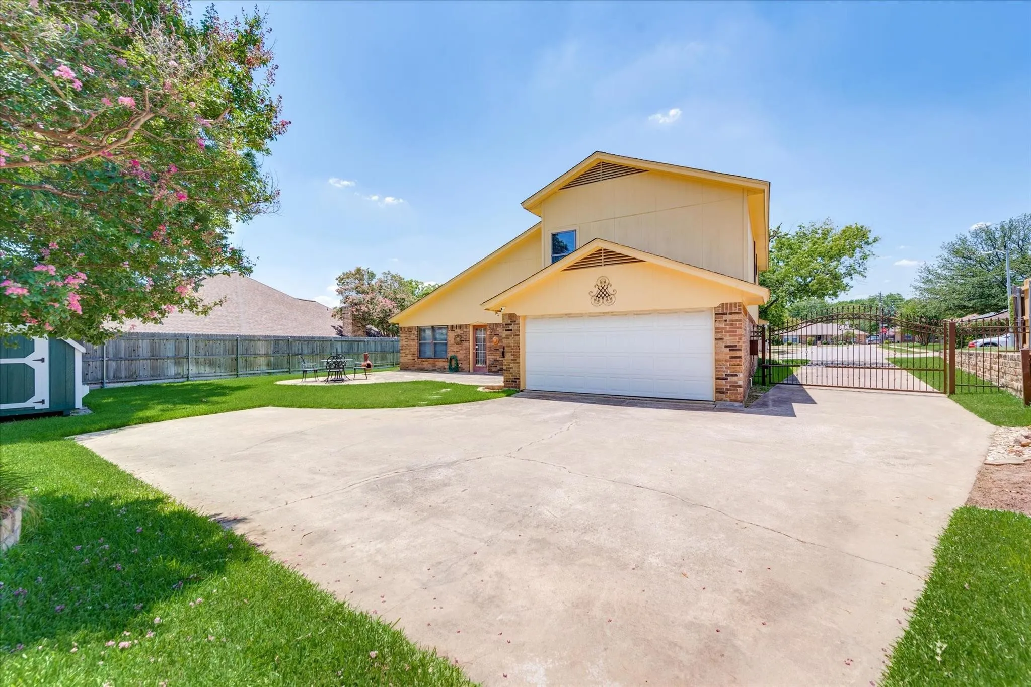 Two-story residence featuring brick and siding exterior, expansive concrete driveway, attached garage, private gated entry, and mature landscaping