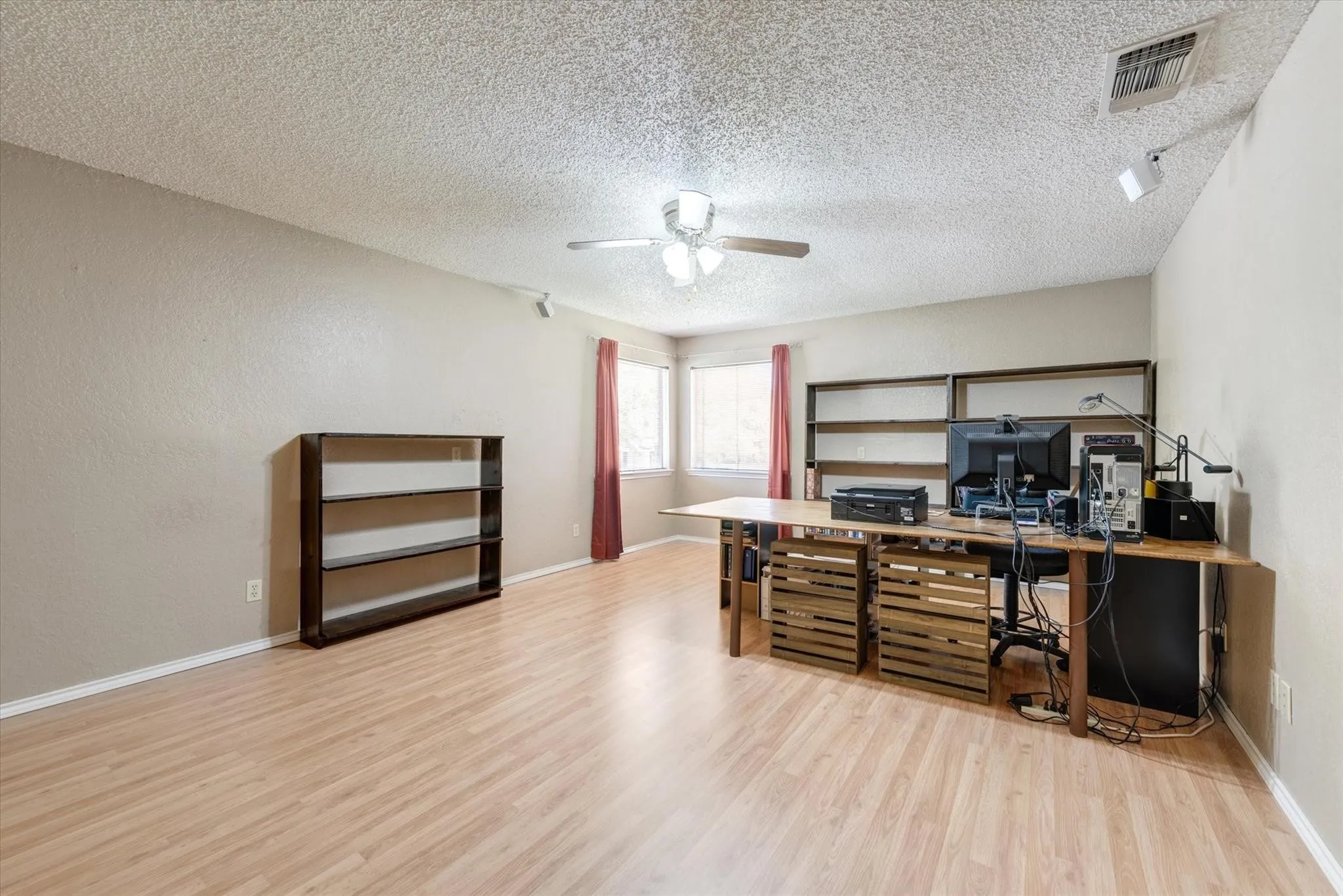 Room featuring wood-finish flooring, built-in wall shelving, and a ceiling-mounted light fixture with fan