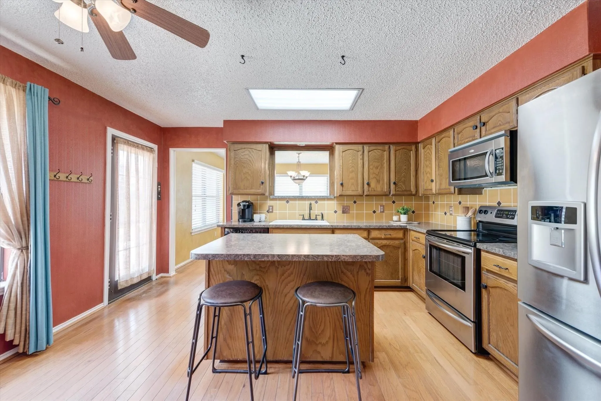 Kitchen featuring wood-finish cabinetry, central island with surface workspace, stainless steel appliances, tiled backsplash, and recessed ceiling lighting