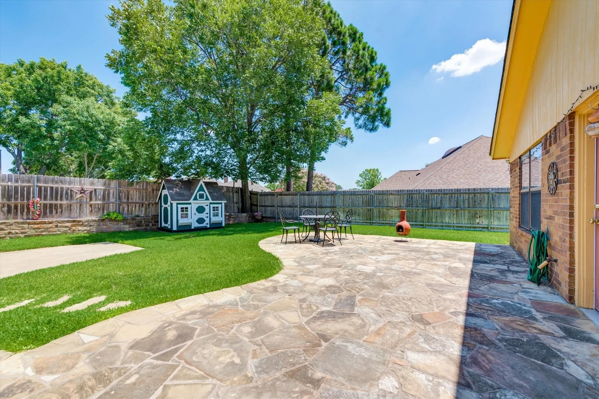 Backyard featuring a stone-paver patio, expansive green lawn, wood fence enclosure, and mature trees