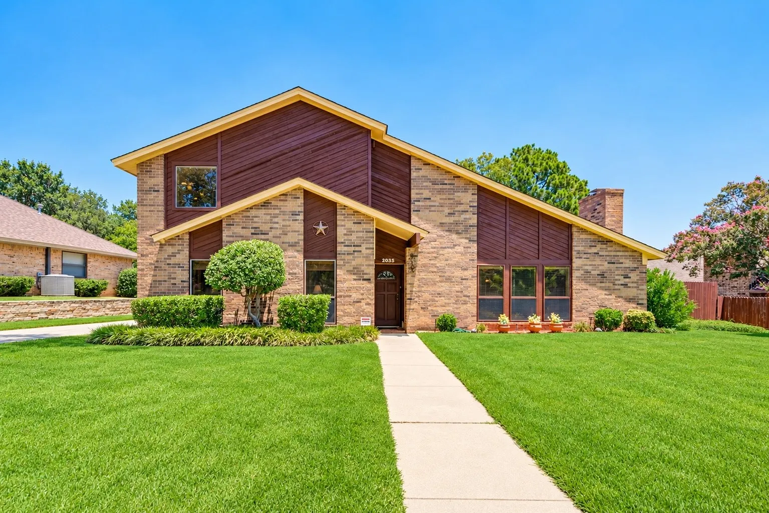 Split-level exterior featuring a brick and wood-panel facade, multi-gabled roofline, brick chimney, and a concrete walkway