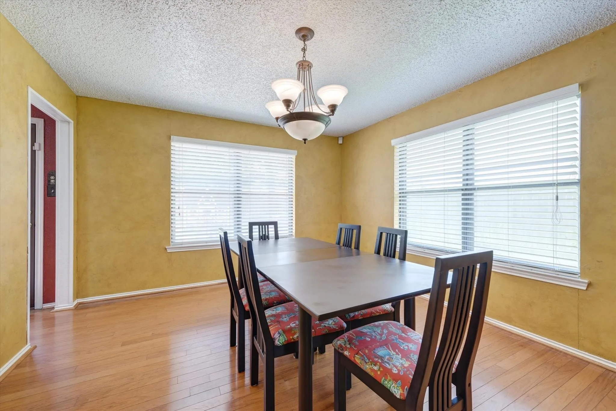 Dining area featuring wood-finish flooring, two large windows with horizontal blinds, and a multi-arm pendant light fixture