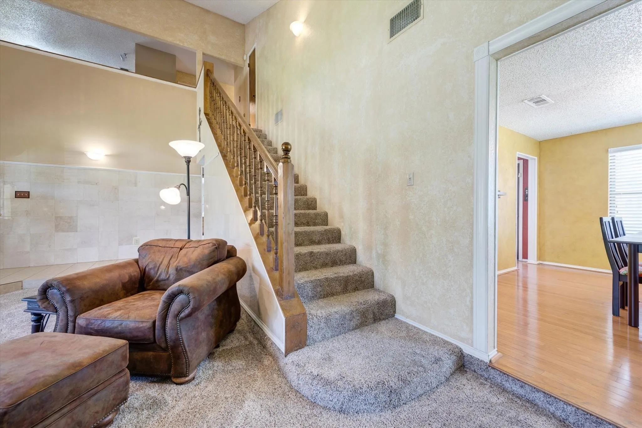 High-ceiling entry featuring a staircase with a wooden banister, wall-mounted lighting, stone-tiled wall accent, and wood-finish flooring