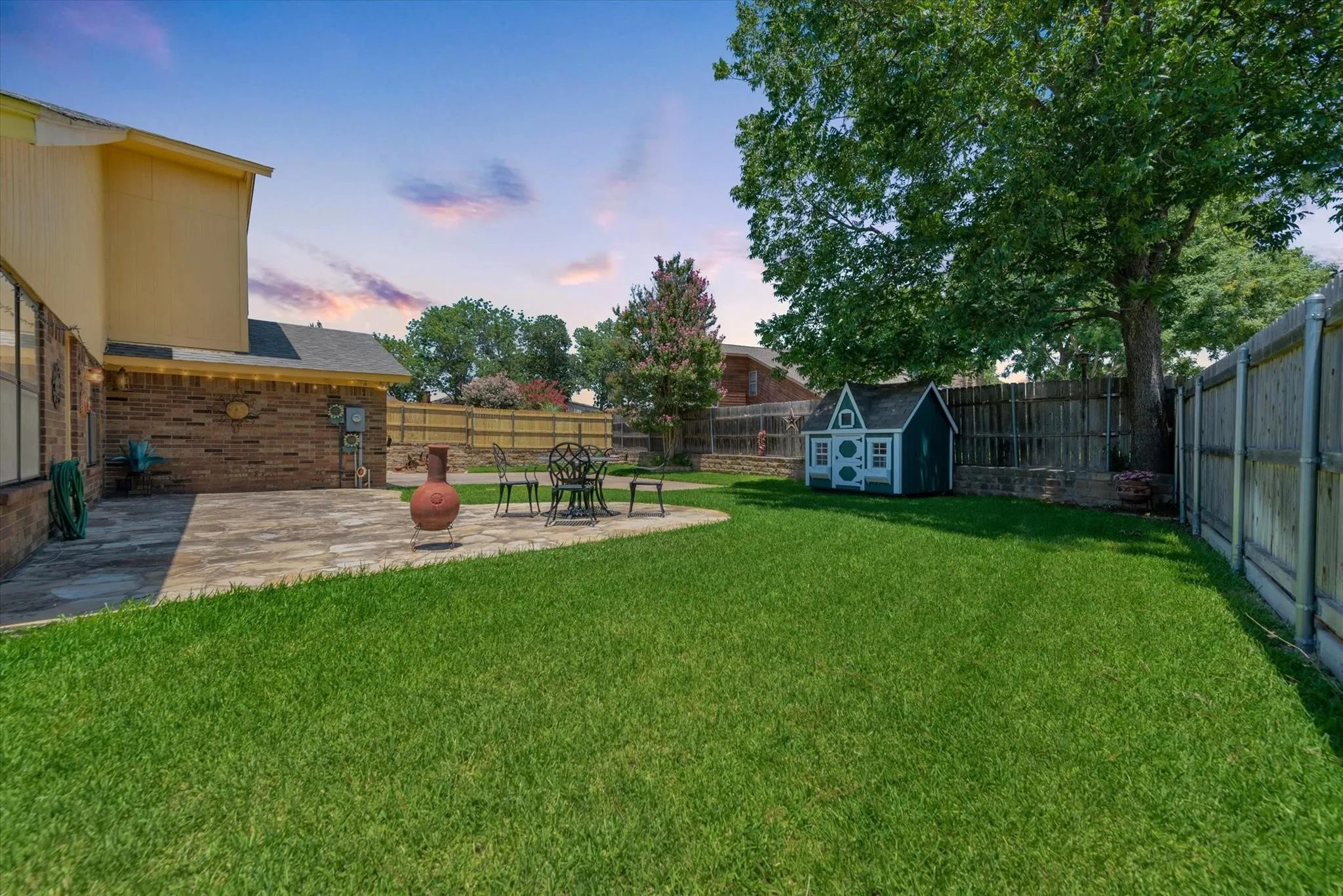 Backyard featuring flagstone patio, manicured lawn, wood fencing, and mature trees
