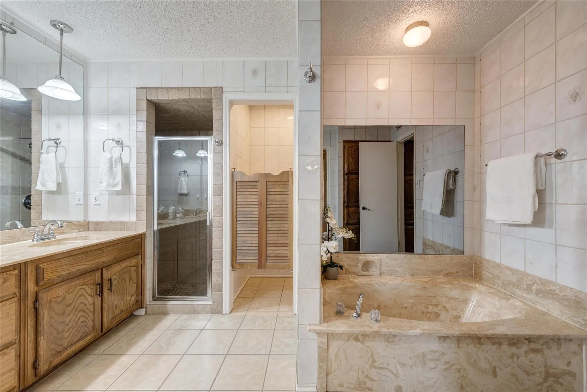 Bathroom featuring dual-sink wooden cabinetry with stone-finish countertops, a walk-in glass-enclosed shower, a built-in soaking tub with stone surround, and ceramic tile flooring