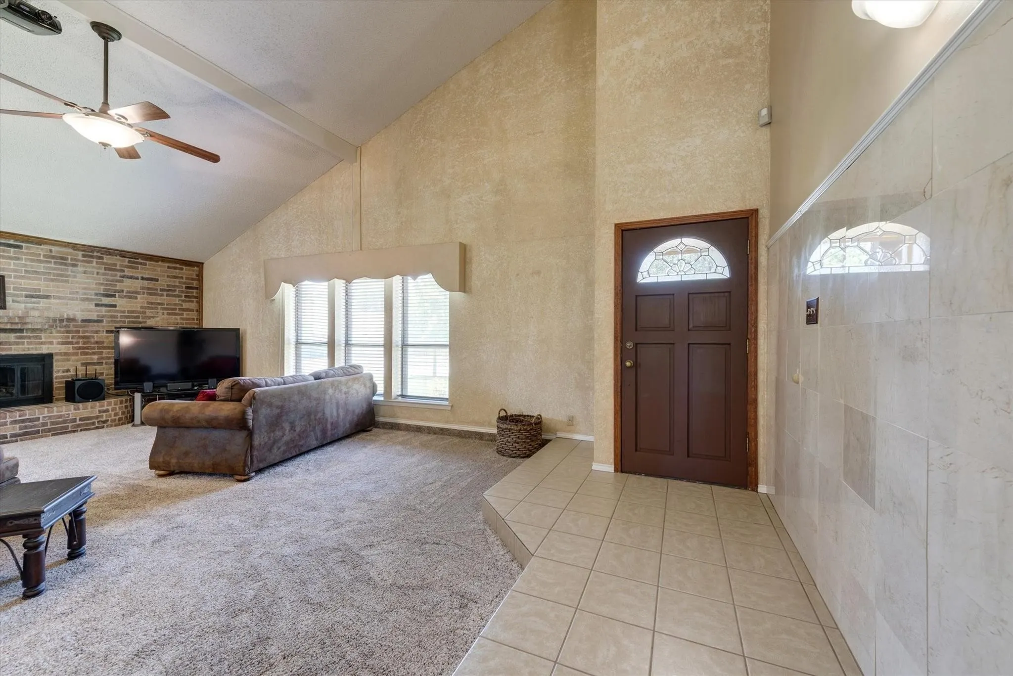 Vaulted ceiling, brick fireplace, tile entryway, and wood-paneled door with decorative glass insert