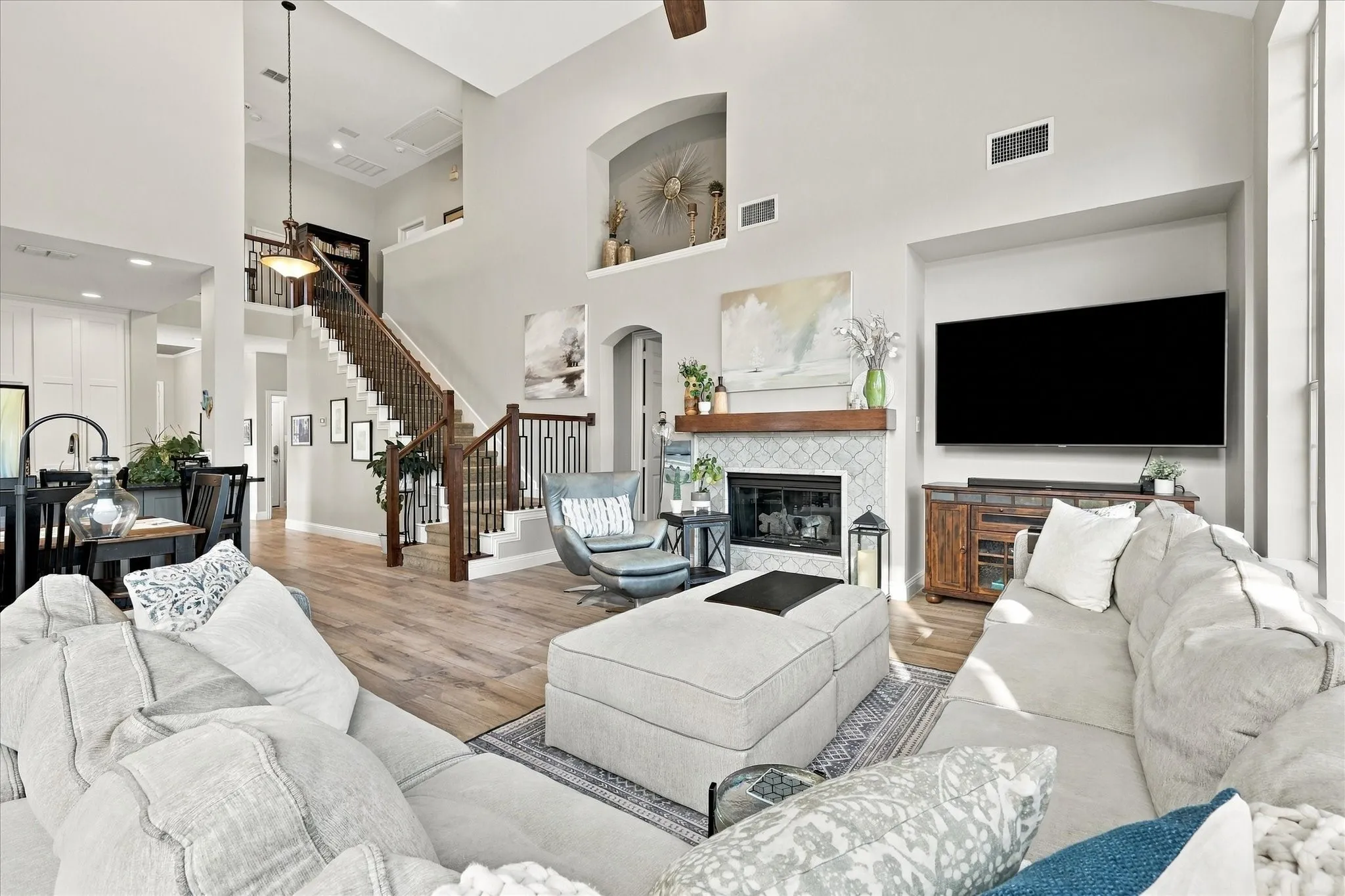 Vaulted ceilings featuring an open staircase with decorative iron balusters, a fireplace with a wood mantel and tile surround, and wood-finish flooring