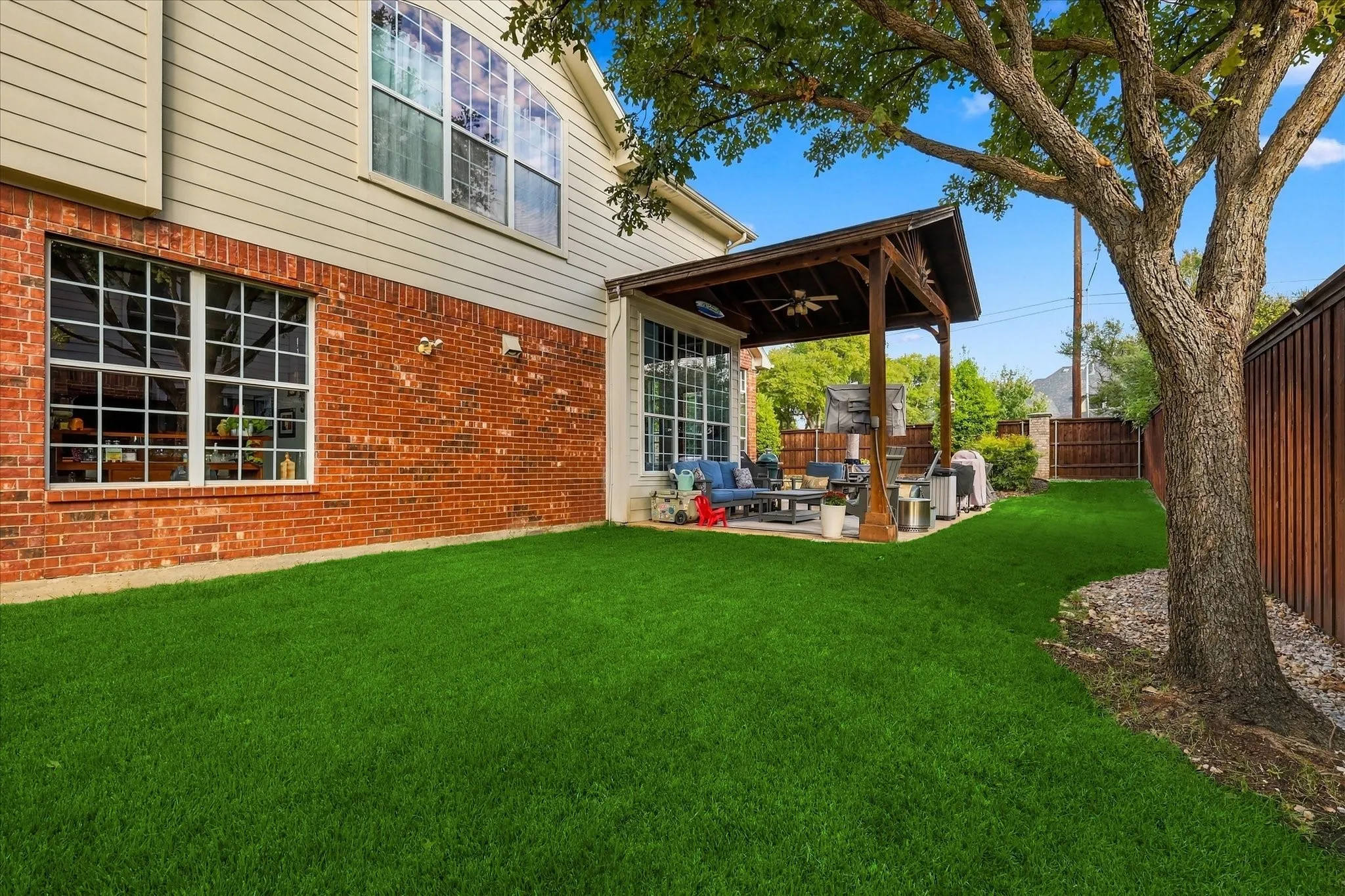 Backyard featuring a covered patio with a ceiling fan, brick and siding exterior, manicured lawn, and mature tree