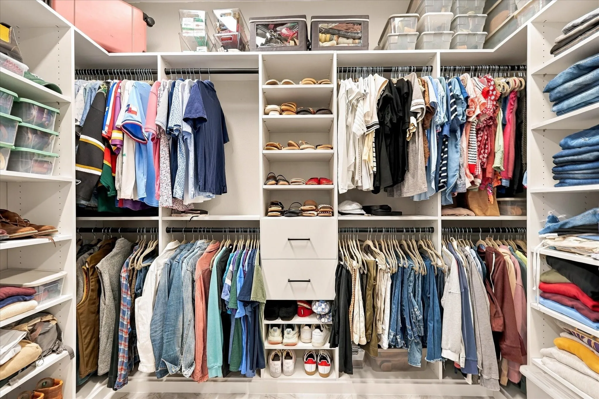 Custom walk-in closet featuring white built-in shelving, dual hanging rods, a central column of open storage cubbies, and two integrated drawers with matte black hardware