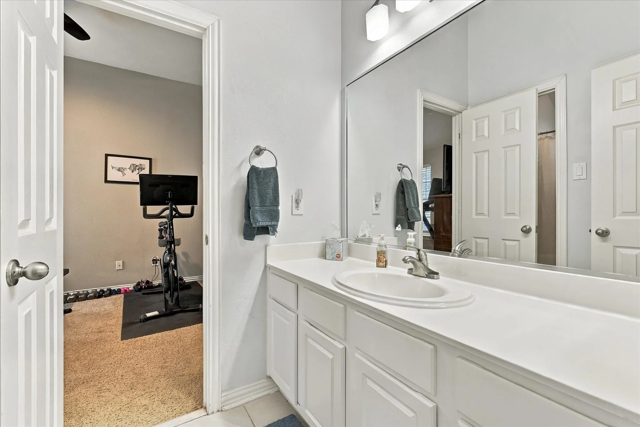 White vanity cabinetry featuring a solid surface countertop, integrated oval basin, metallic hardware, and an expansive wall-mounted mirror